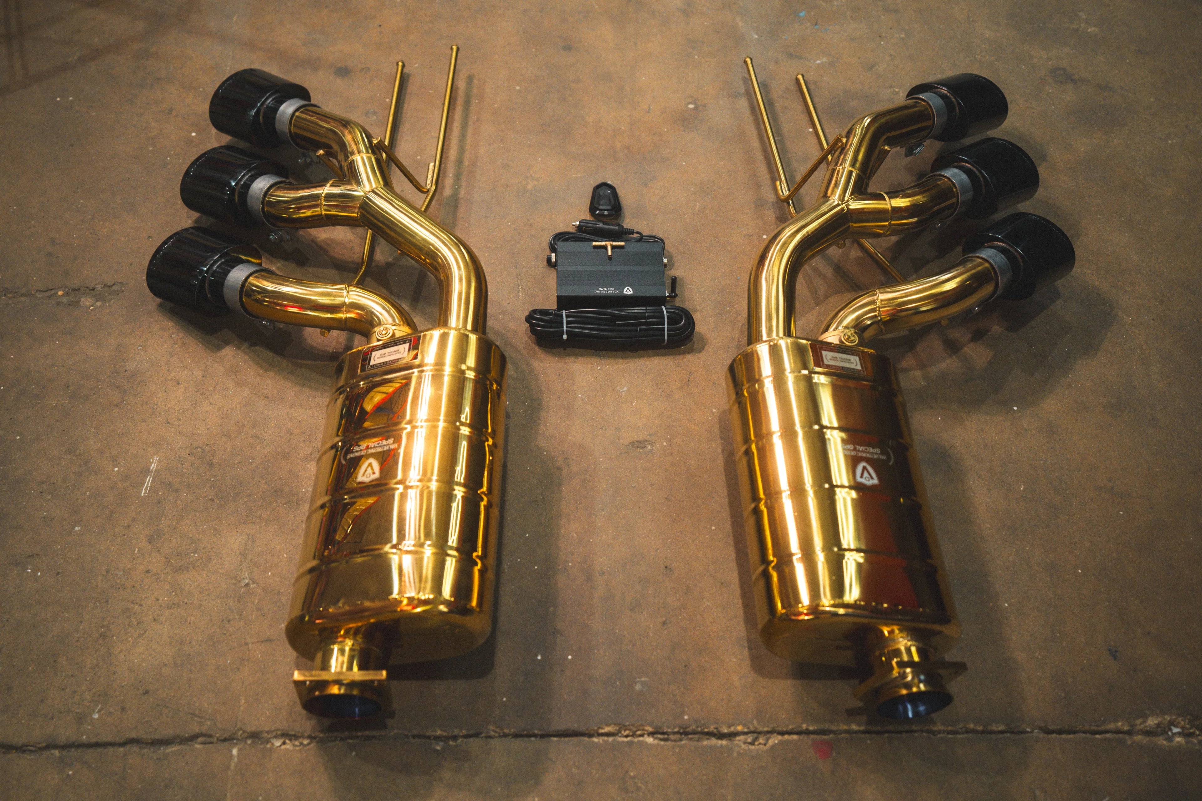 Rear view of the exhaust system components showing the inlet flanges of the gold mufflers and the triple exhaust tip configuration.