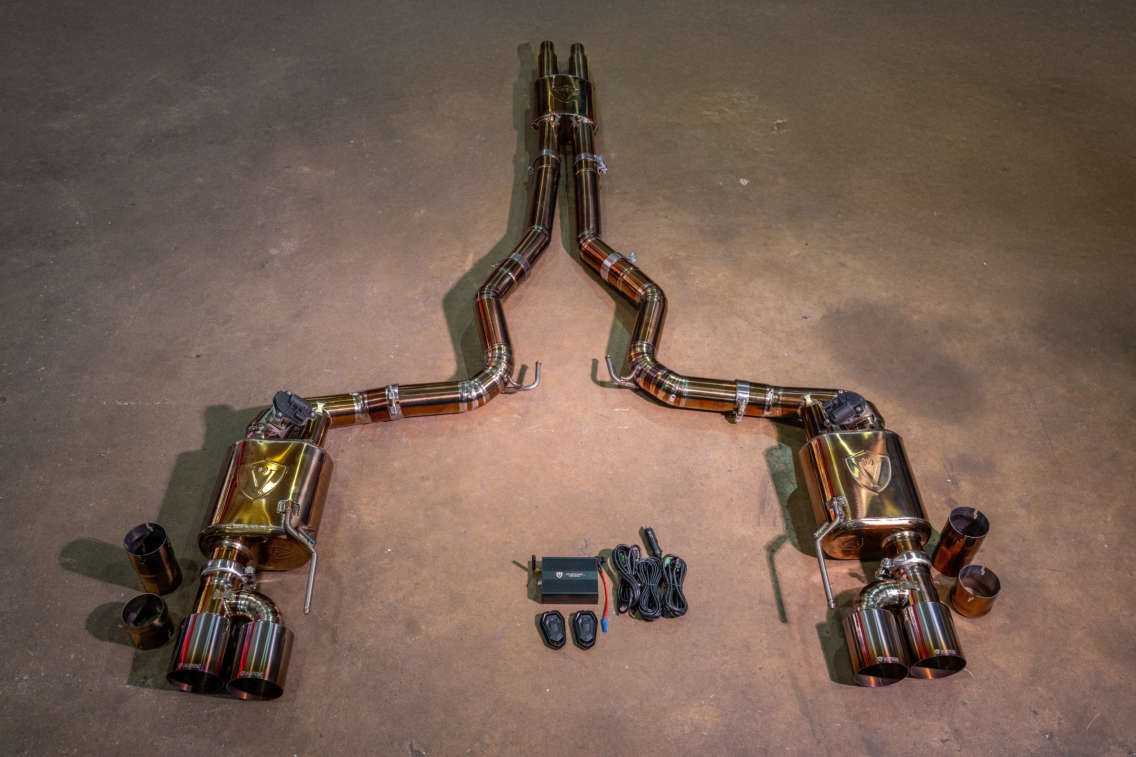 An overhead view of a heat-treated version of the exhaust system, displaying a bronze-tinted finish on the piping, mufflers with engraved logos, and quad exhaust tips.