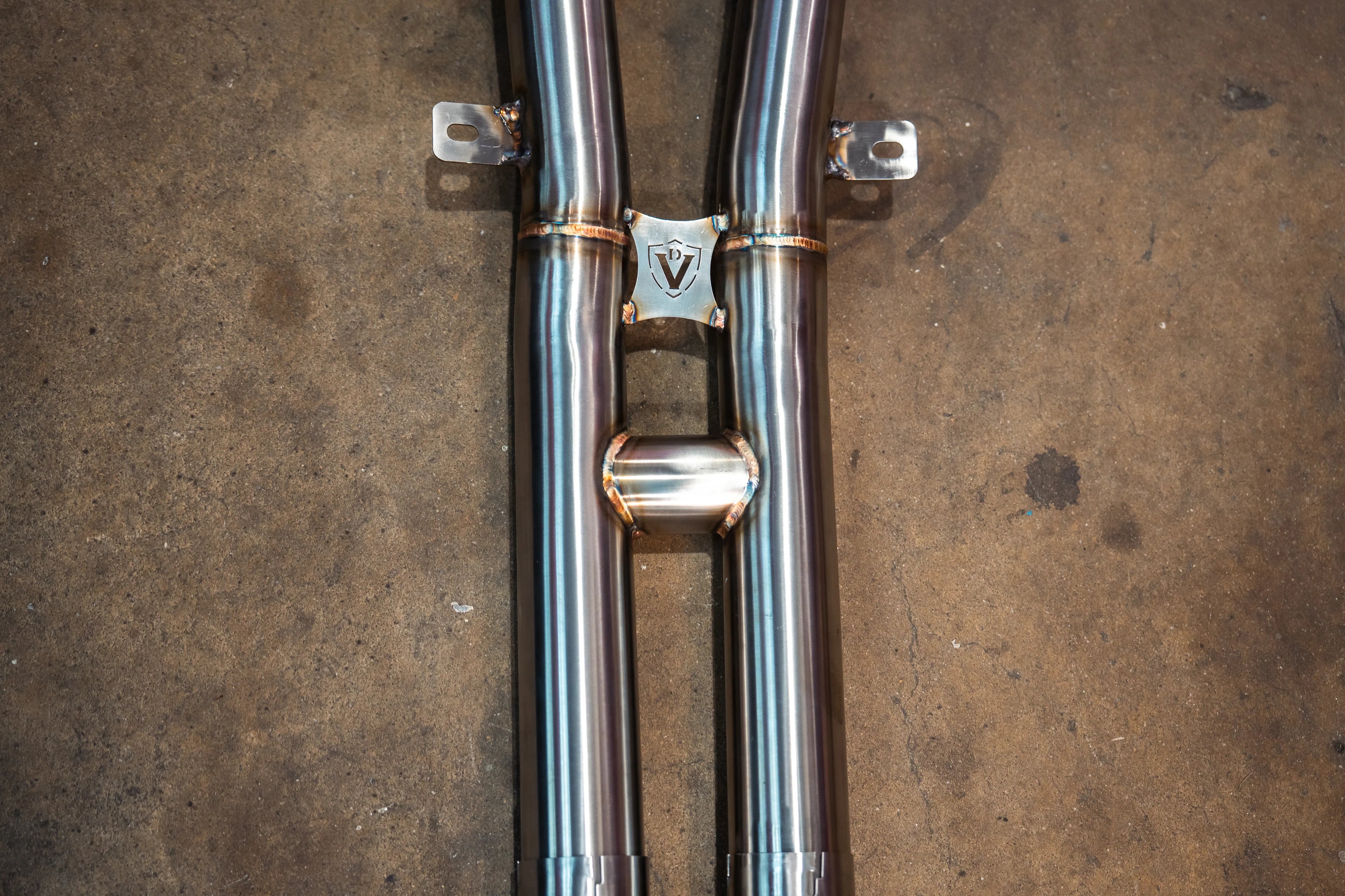 Close-up of the titanium crossover section featuring a Valvetronic Designs logo shield and support brackets.