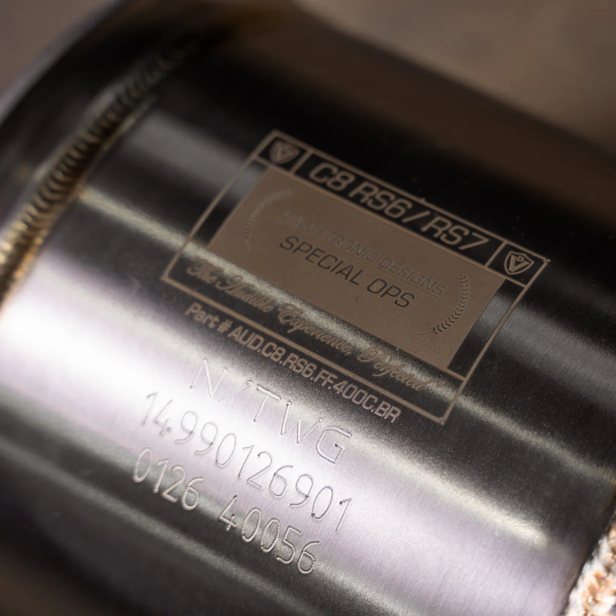Close-up of Valvetronic Designs Special Ops identification plate on Audi C8 RS6/RS7 catted downpipe, showing part number AUD.C8.RS6.FF.400C.BR and precision TIG welding.
