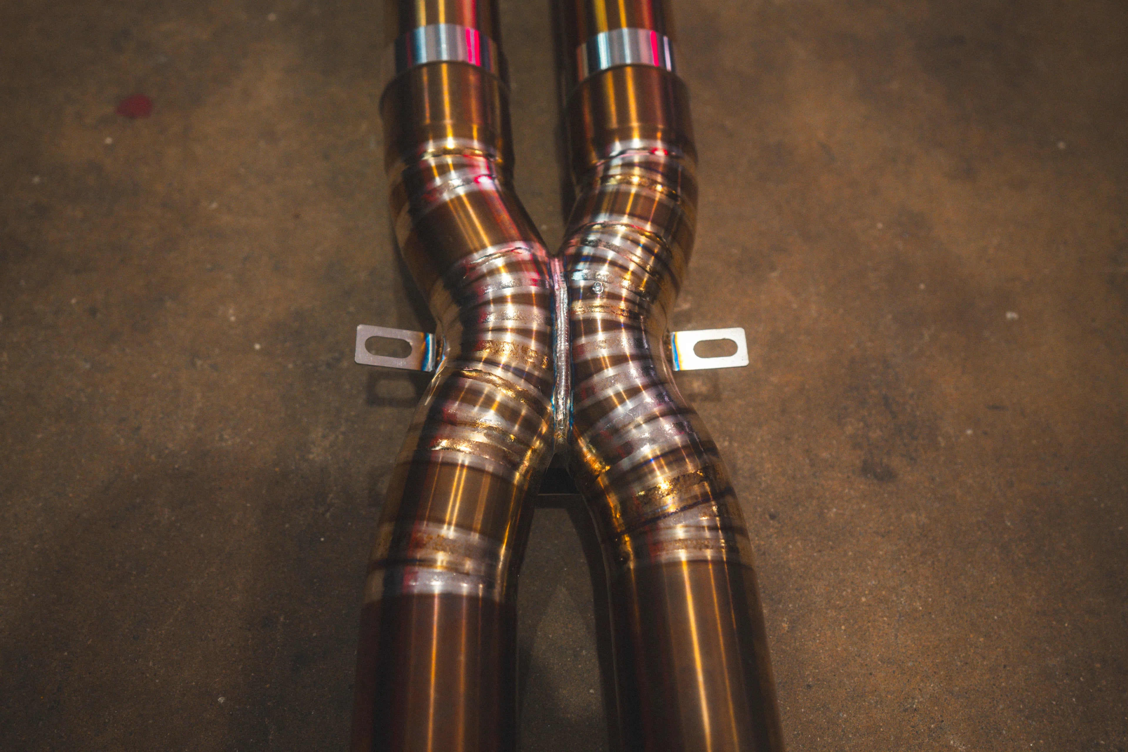 A detailed shot of the exhaust system's X-pipe merge point, showing the precision weld beads on the titanium piping.