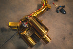 A side view of one gold-plated muffler assembly showing the vacuum-actuated valve, mounting brackets, and the authenticity plaque.