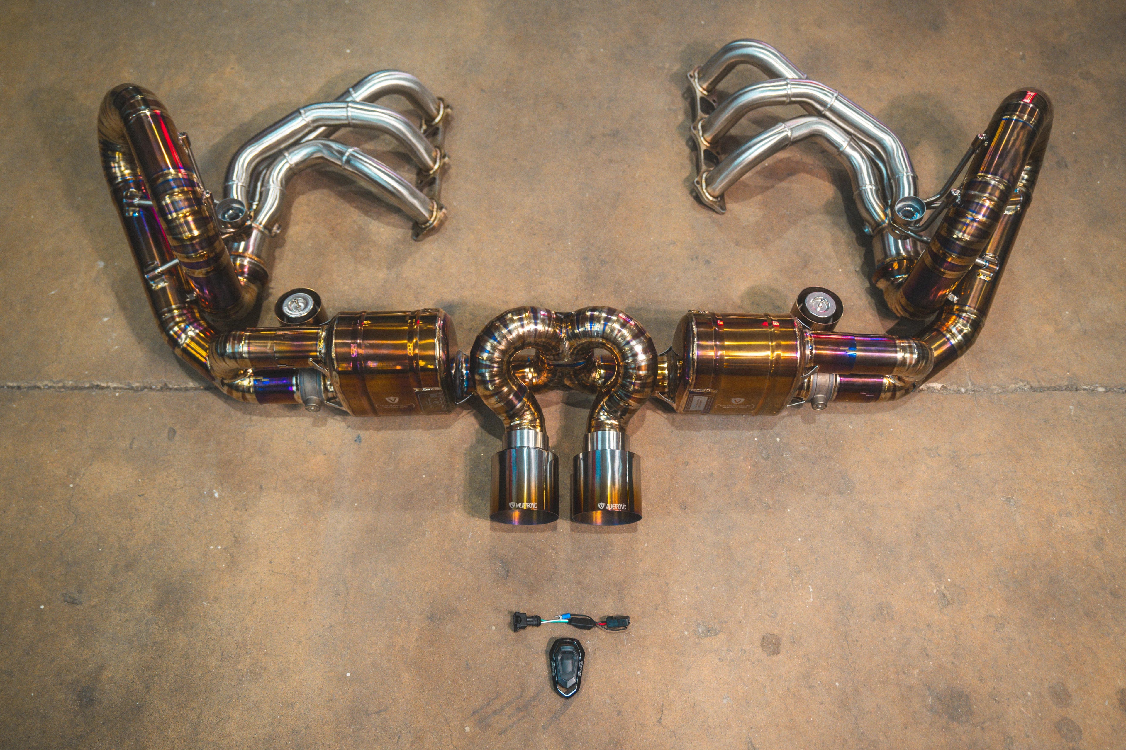 Full assembly of the titanium valved exhaust system connected to heat-shielded headers, highlighting the burnt-finish piping and dual tips.