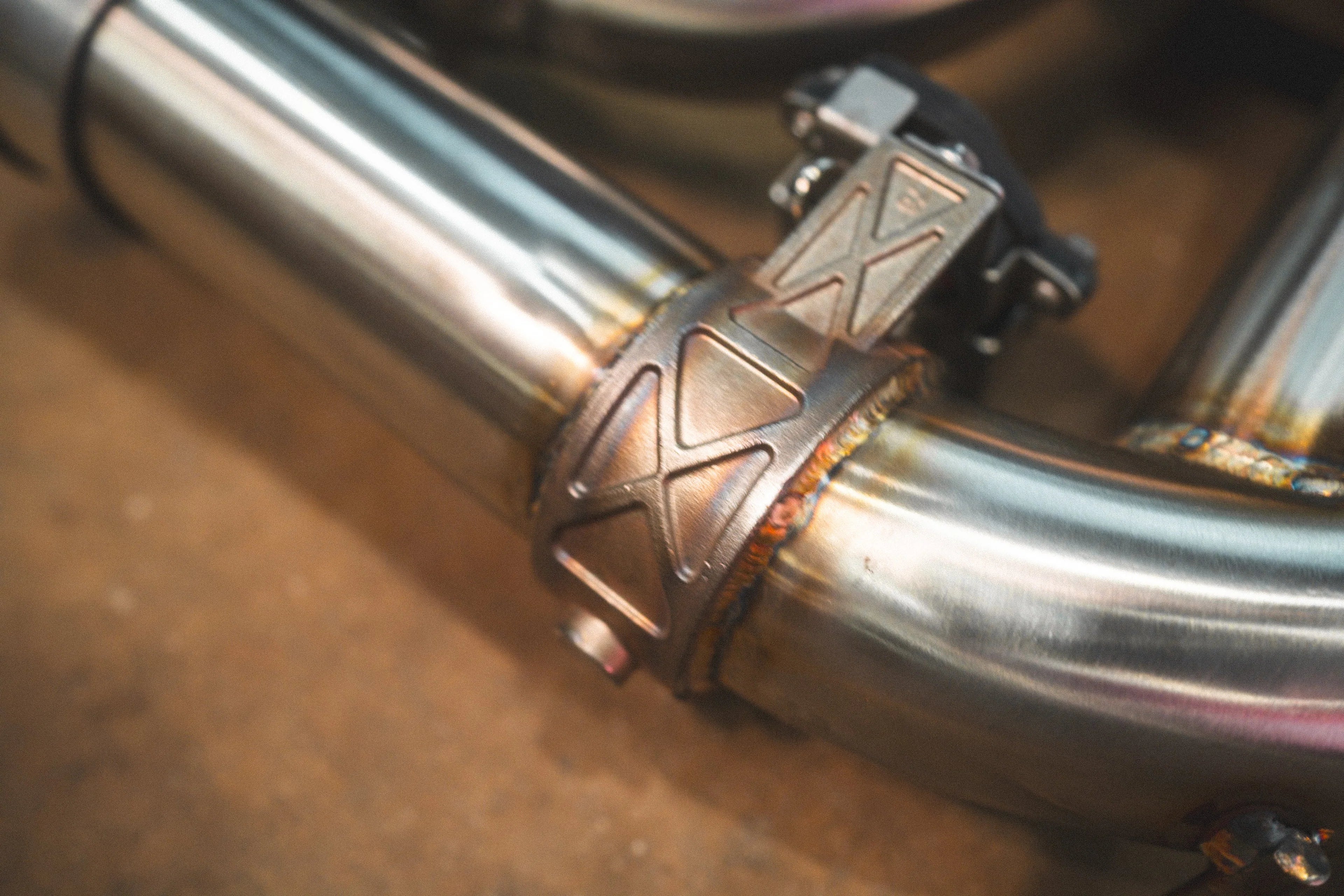 Extreme close-up of a high-quality TIG weld and a structural reinforcement brace on the stainless steel exhaust piping.