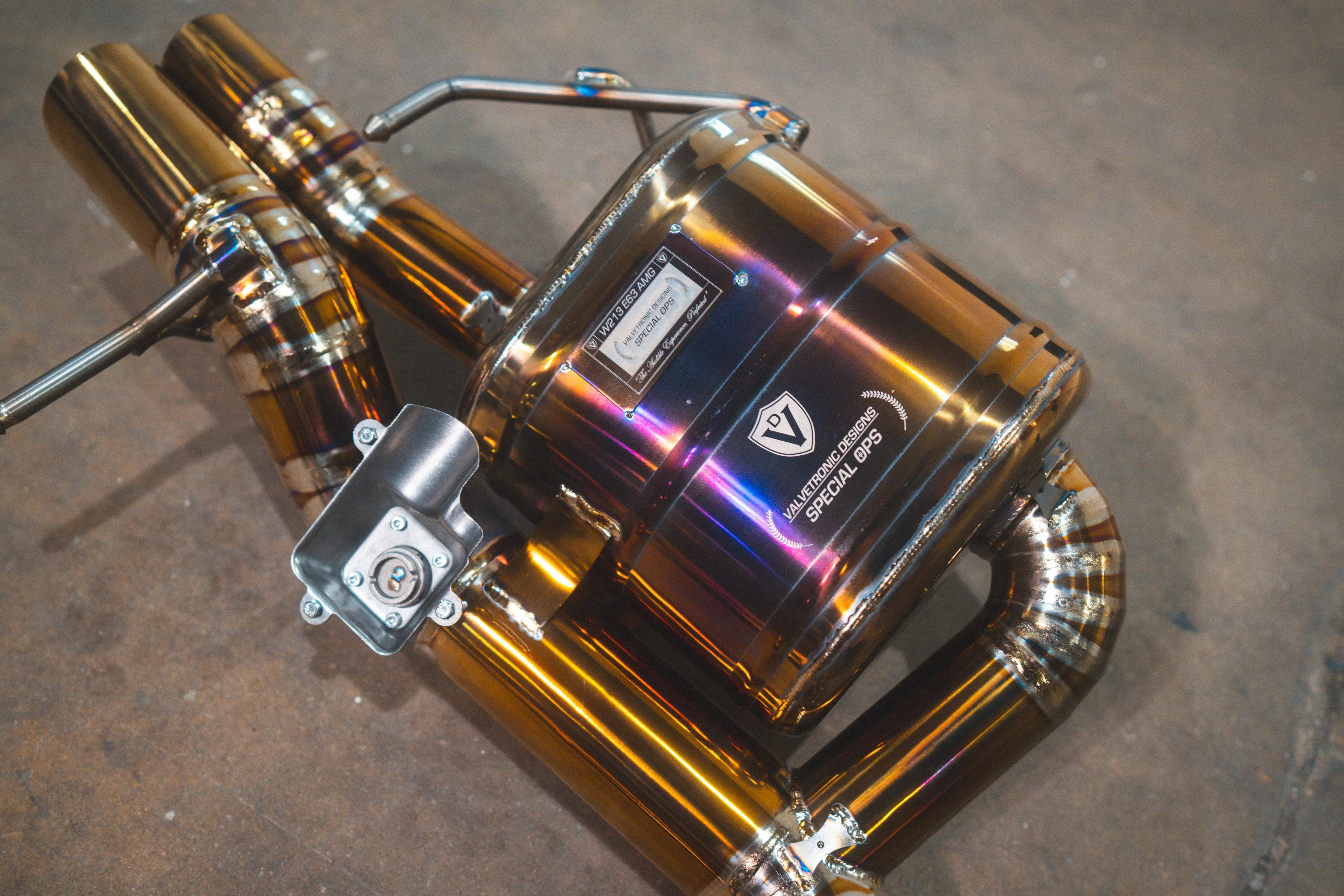 Detailed angled view of the titanium-finish muffler displaying the "Valvetronic Designs Special Ops" logo and an electronic valve motor mount.