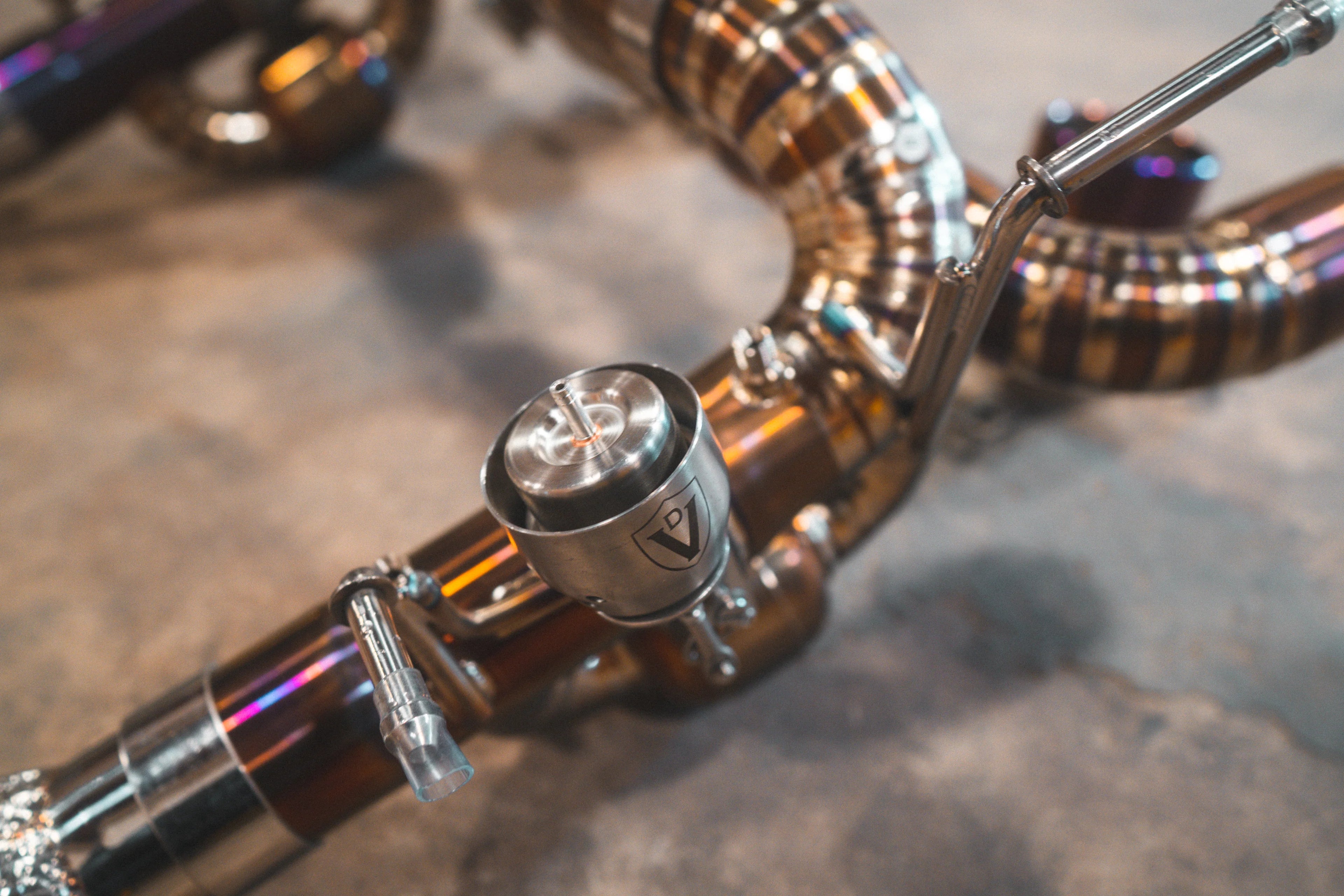 An angled overhead view of the full exhaust kit including headers, mid-pipes with heat shielding, and the gold muffler unit.