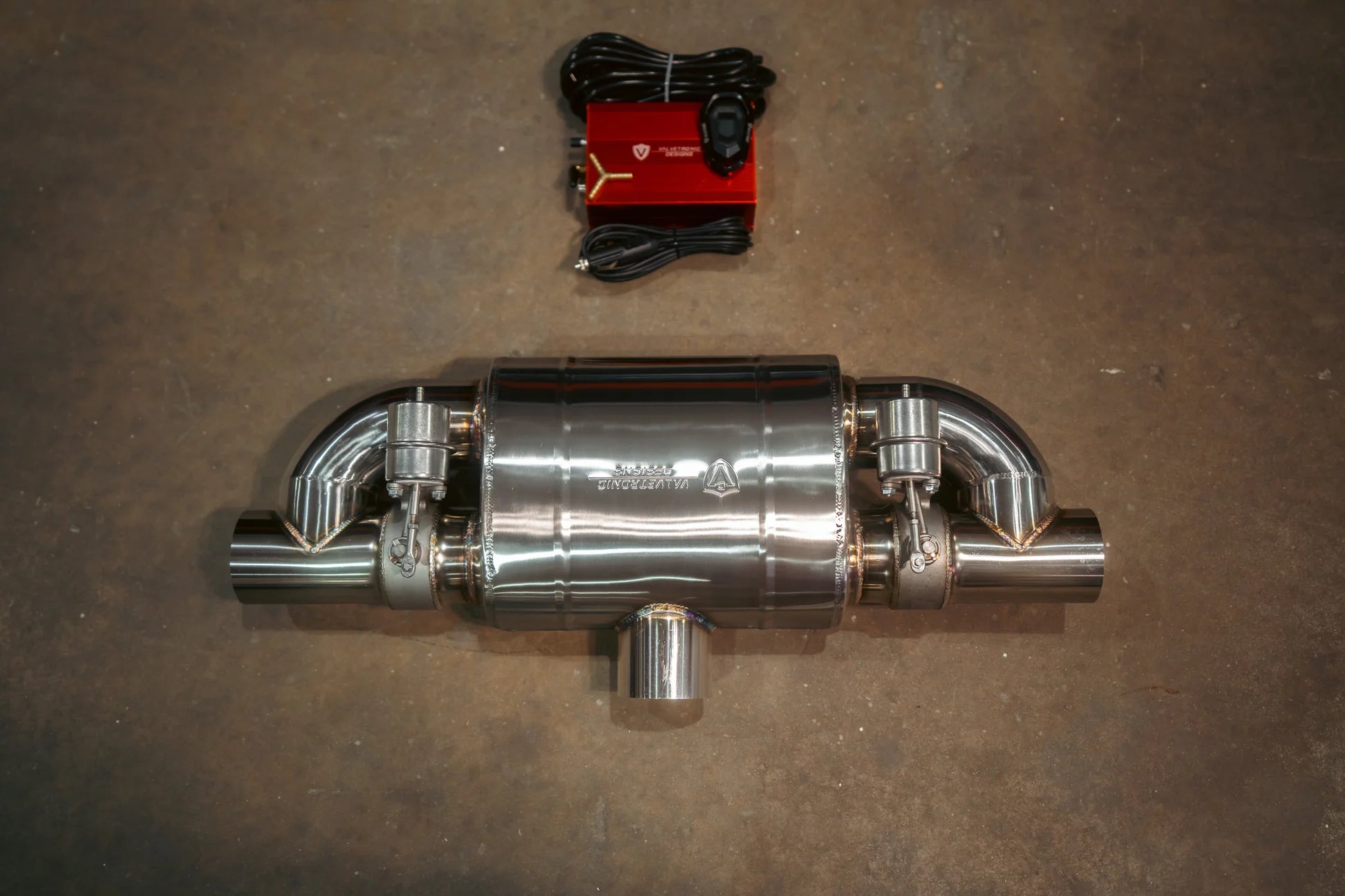 A single stainless steel t style muffler with dual valve actuators positioned horizontally below a red electronic control box and coiled wiring.