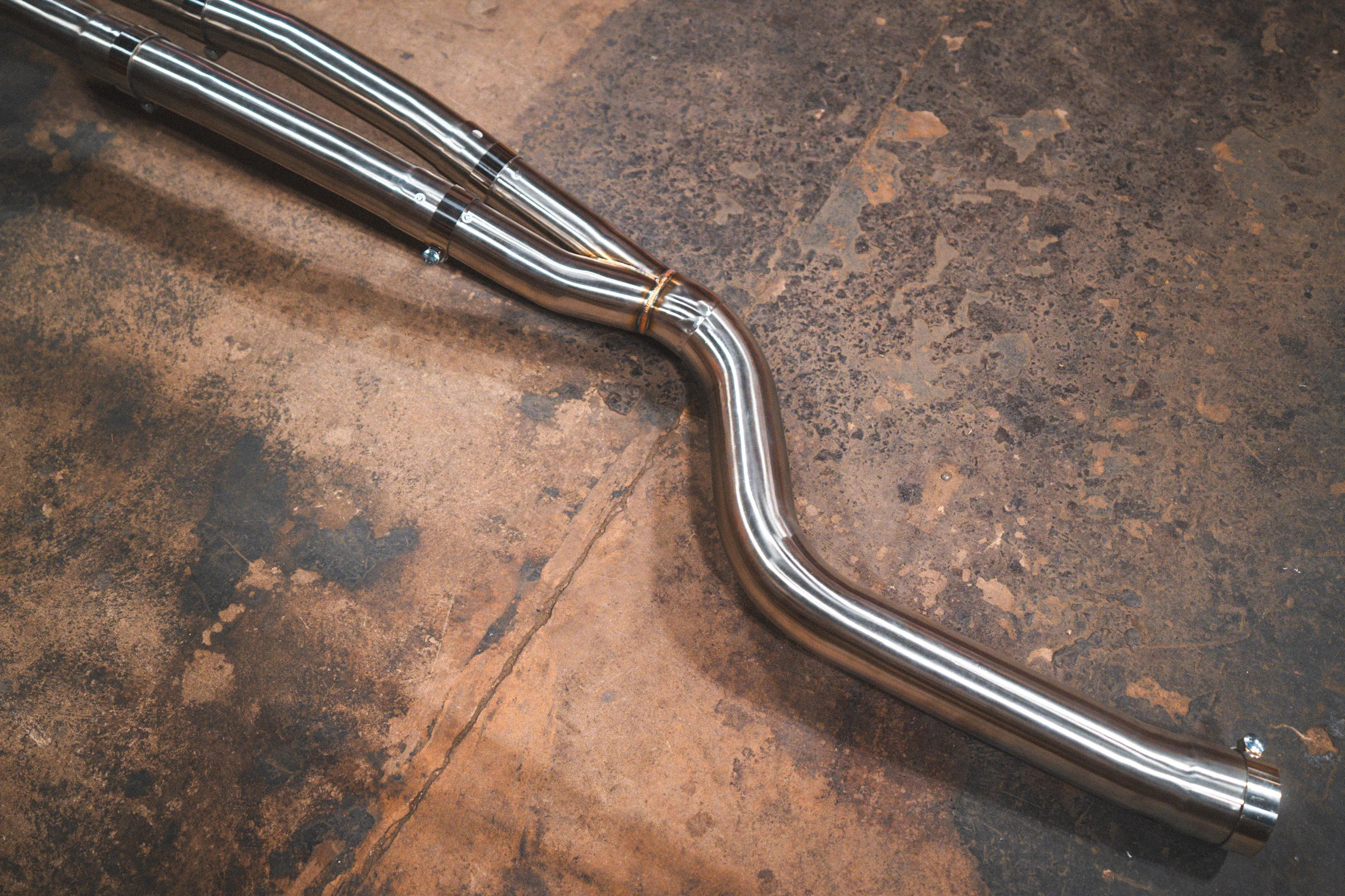 A section of stainless steel mid-piping with visible welds and brackets resting on a brown concrete floor.