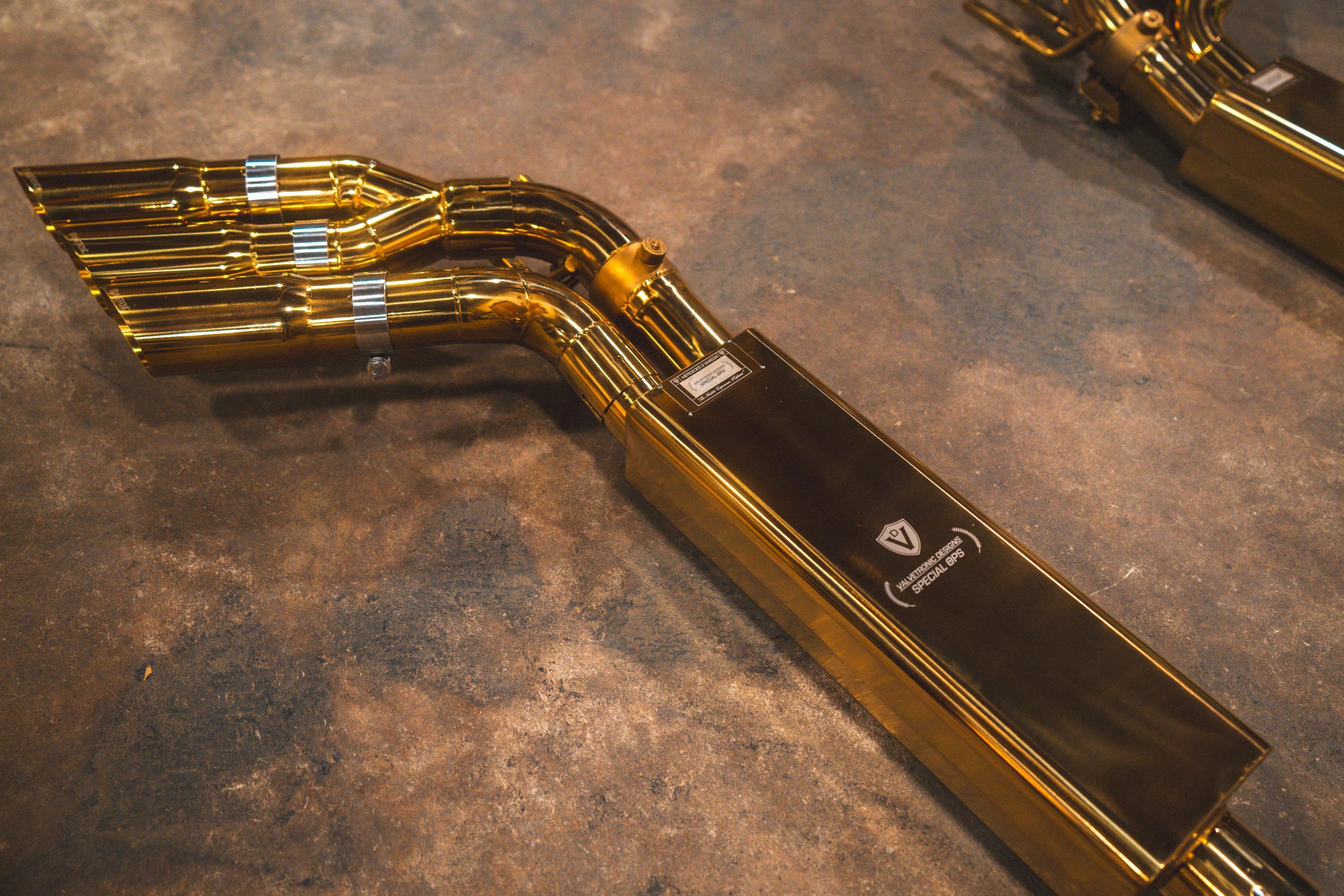 Rear-facing view of the gold mufflers showing the exhaust inlet flanges and the detailed triple-exit piping.