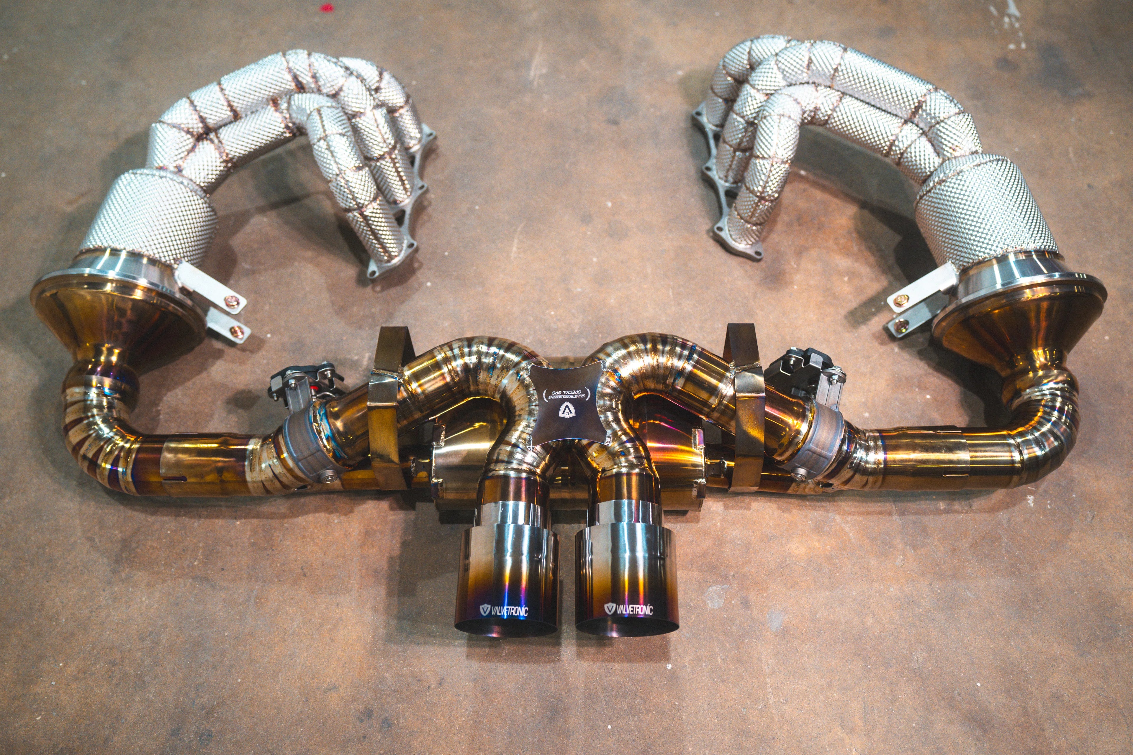 A view of the valved exhaust system connected to heat-shielded headers, highlighting the intricate weld patterns and titanium finish.