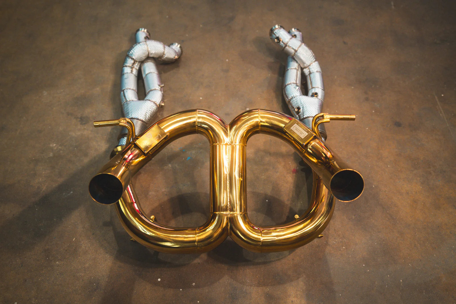 Bottom-up view of the gold exhaust system showing the two main outlet pipes and the textured silver heat shielding on the secondary piping.