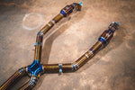 Close-up of the upper titanium exhaust piping featuring high-quality pie-cut welds, blue heat-tinted resonators, and exhaust flanges.