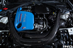 Black carbon fiber charge pipes with smooth curved design installed in BMW M3 engine bay around blue engine cover - Eventuri charge pipes for BMW M3