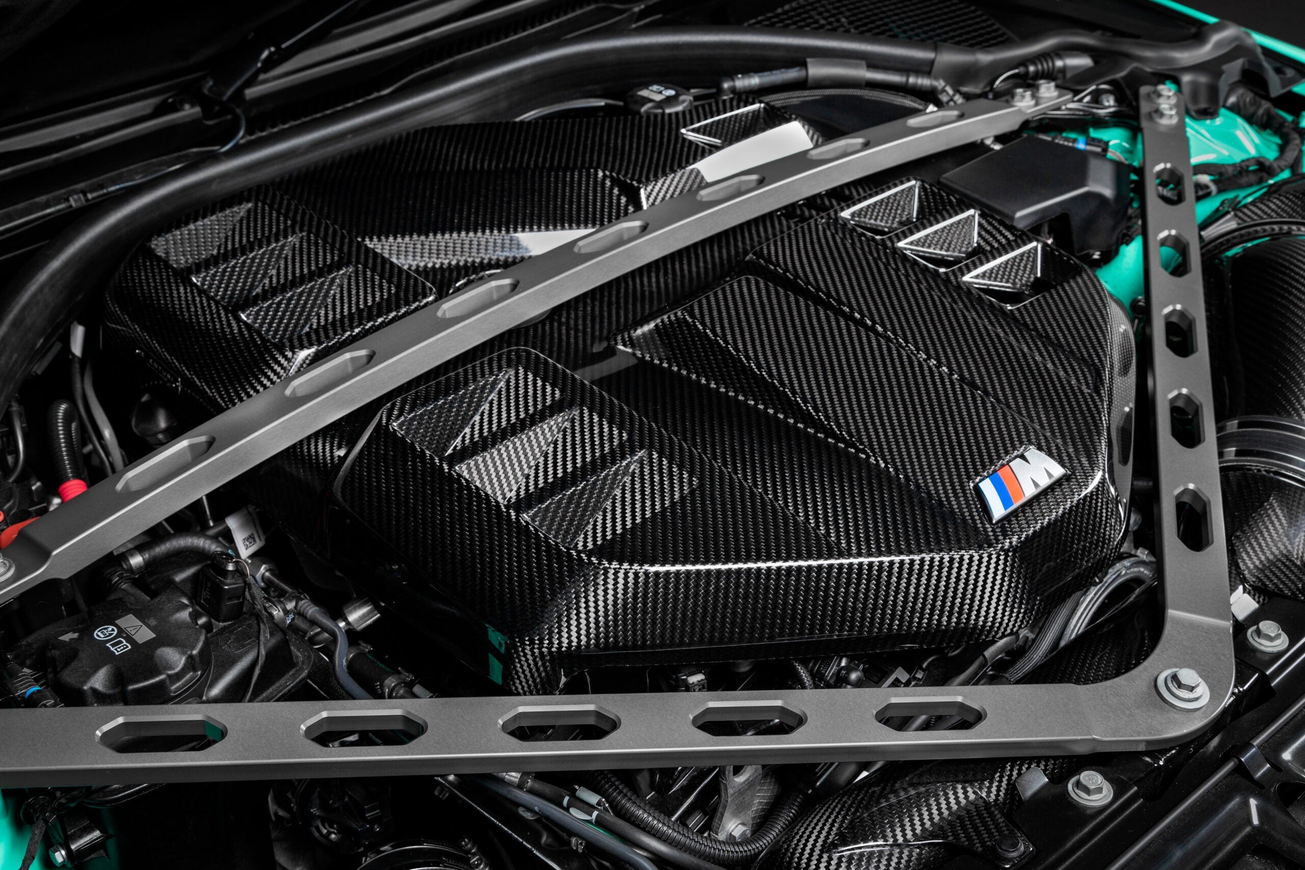 Installed Eventuri gloss carbon S58 cover with M badge, seen between the strut brace arms