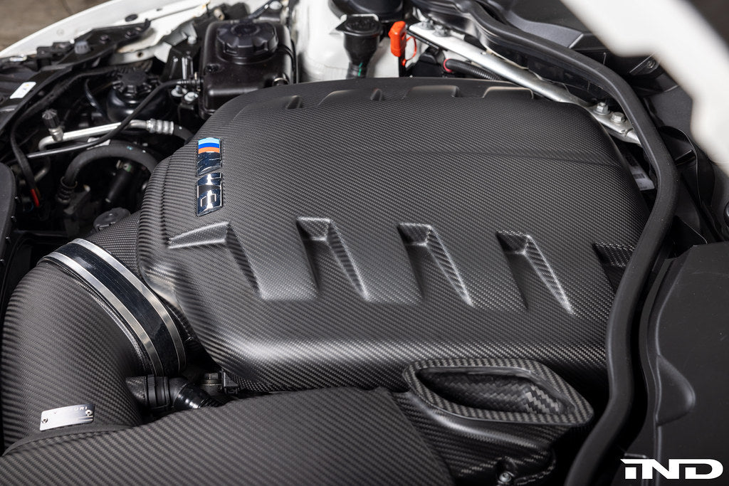 Carbon fiber inlet plenum with ribbed surface pattern installed in BMW M3 engine bay with white IND logo watermark - Eventuri inlet plenum for BMW M3