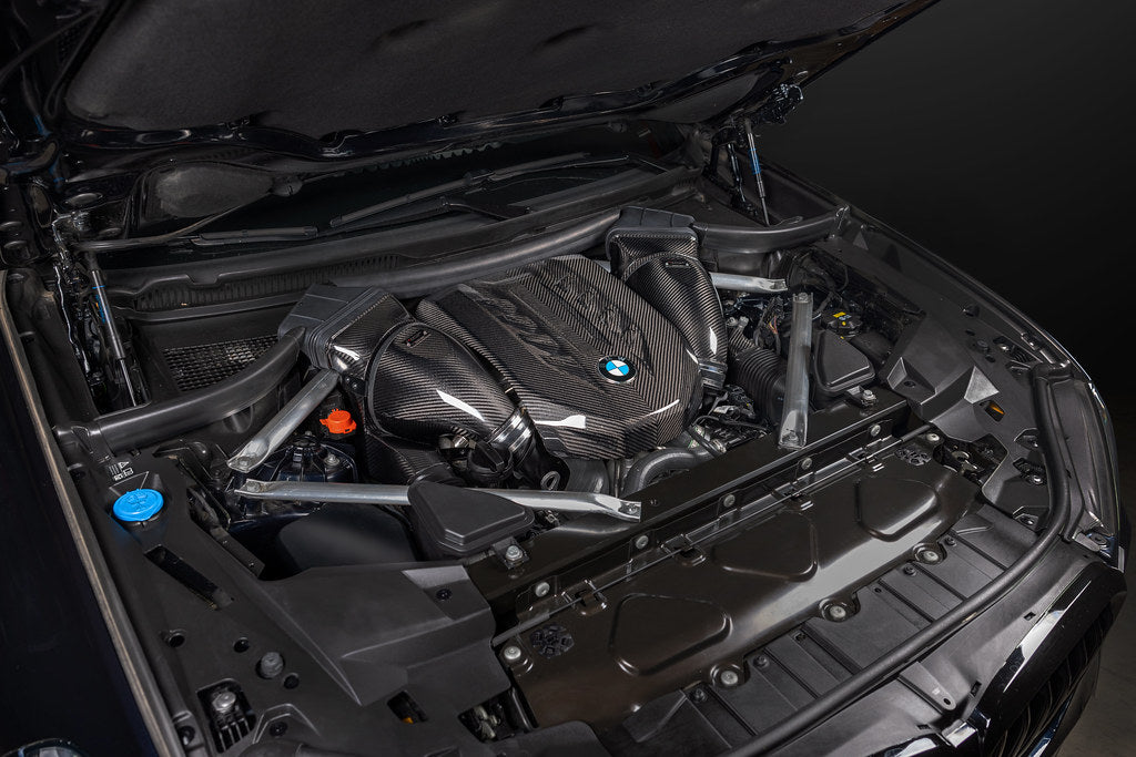 Carbon fiber engine cover and intake components installed in BMW engine bay with hood open - Eventuri intake for BMW X5 M50i