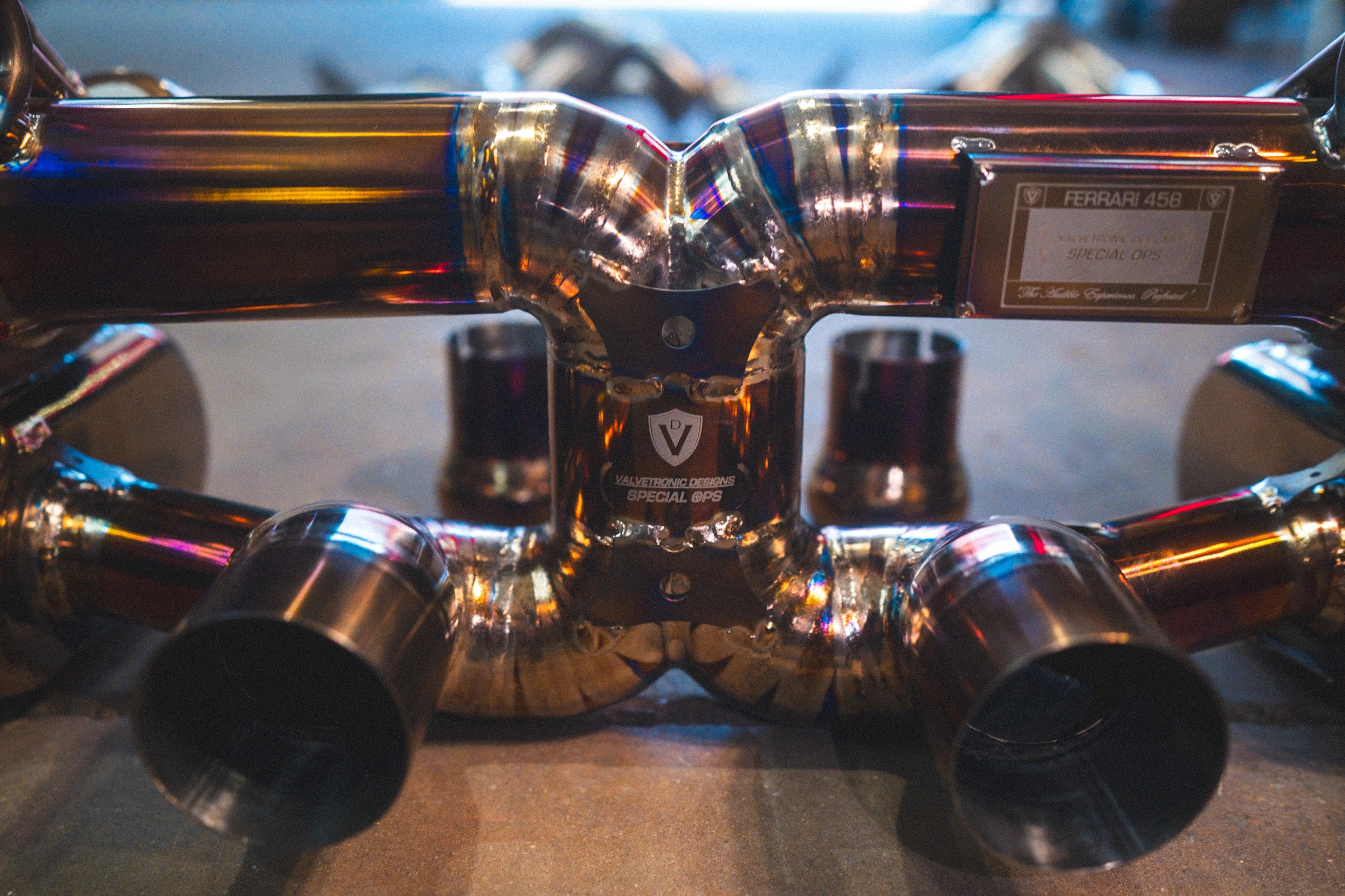 A close-up front view of the exhaust X-pipe section featuring the Valvetronic Designs Special Ops logo and dual exhaust tips.