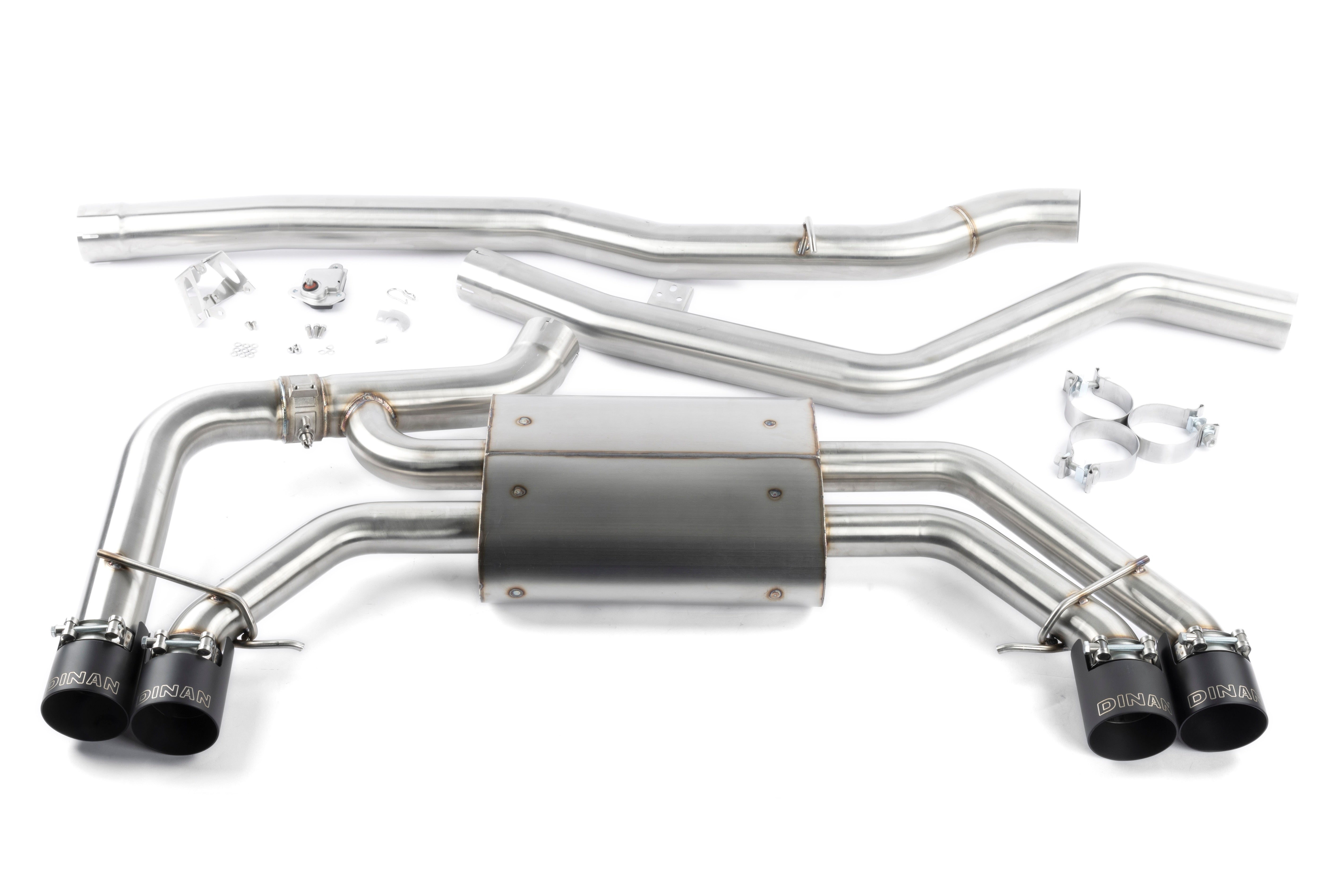 A studio product shot on a white background showing the complete Dinan Valved Cat-Back Exhaust System for the BMW X3 M40i. The system is laid out to show the brushed T304 stainless steel construction, featuring a large single mid-pipe that connects to a rear muffler with quad black ceramic coated exhaust tips.
