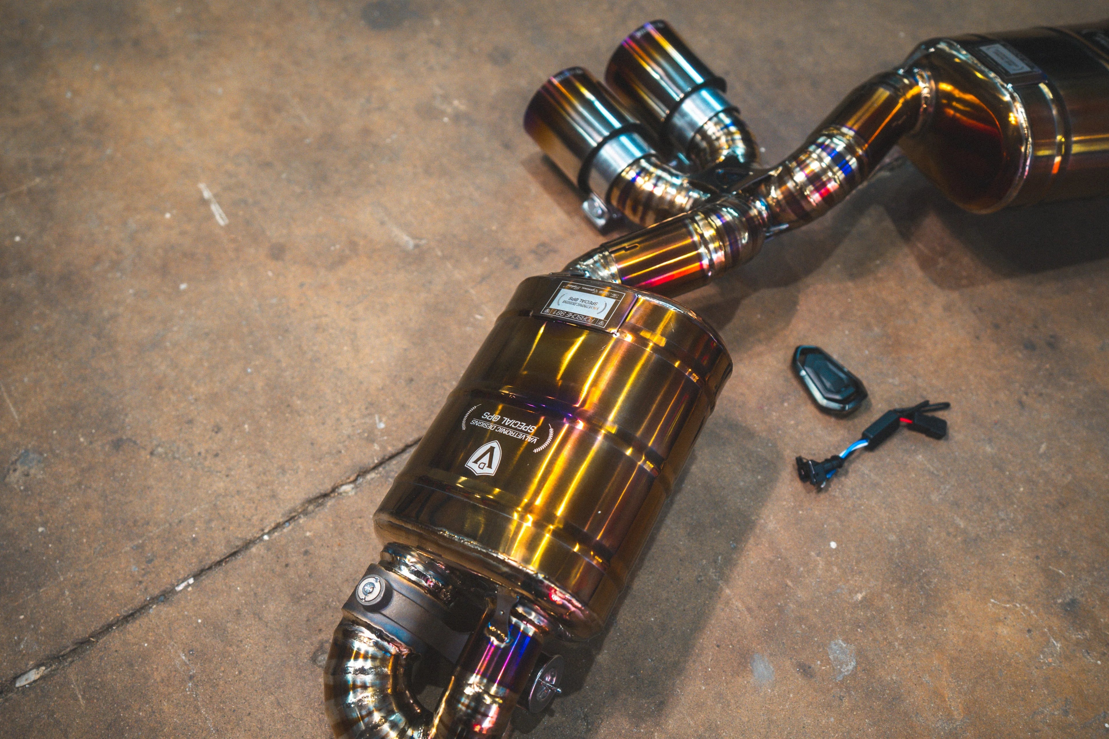 An angled side view of the dual muffler setup, highlighting the electronic valve actuators and the uniform gold-tone finish of the piping.