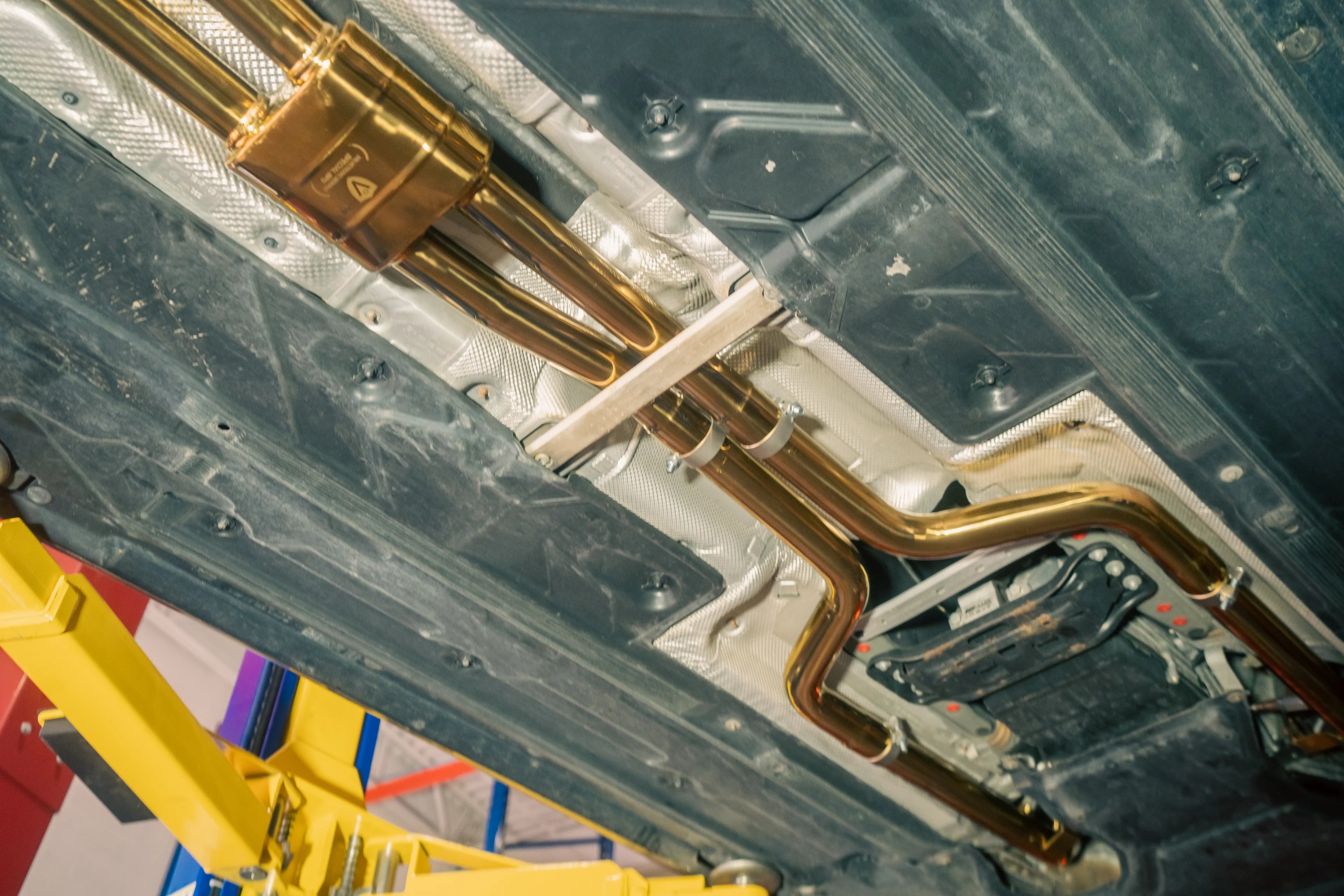 Perspective view from under the vehicle showing the long runs of gold-plated exhaust piping extending toward the front of the car.