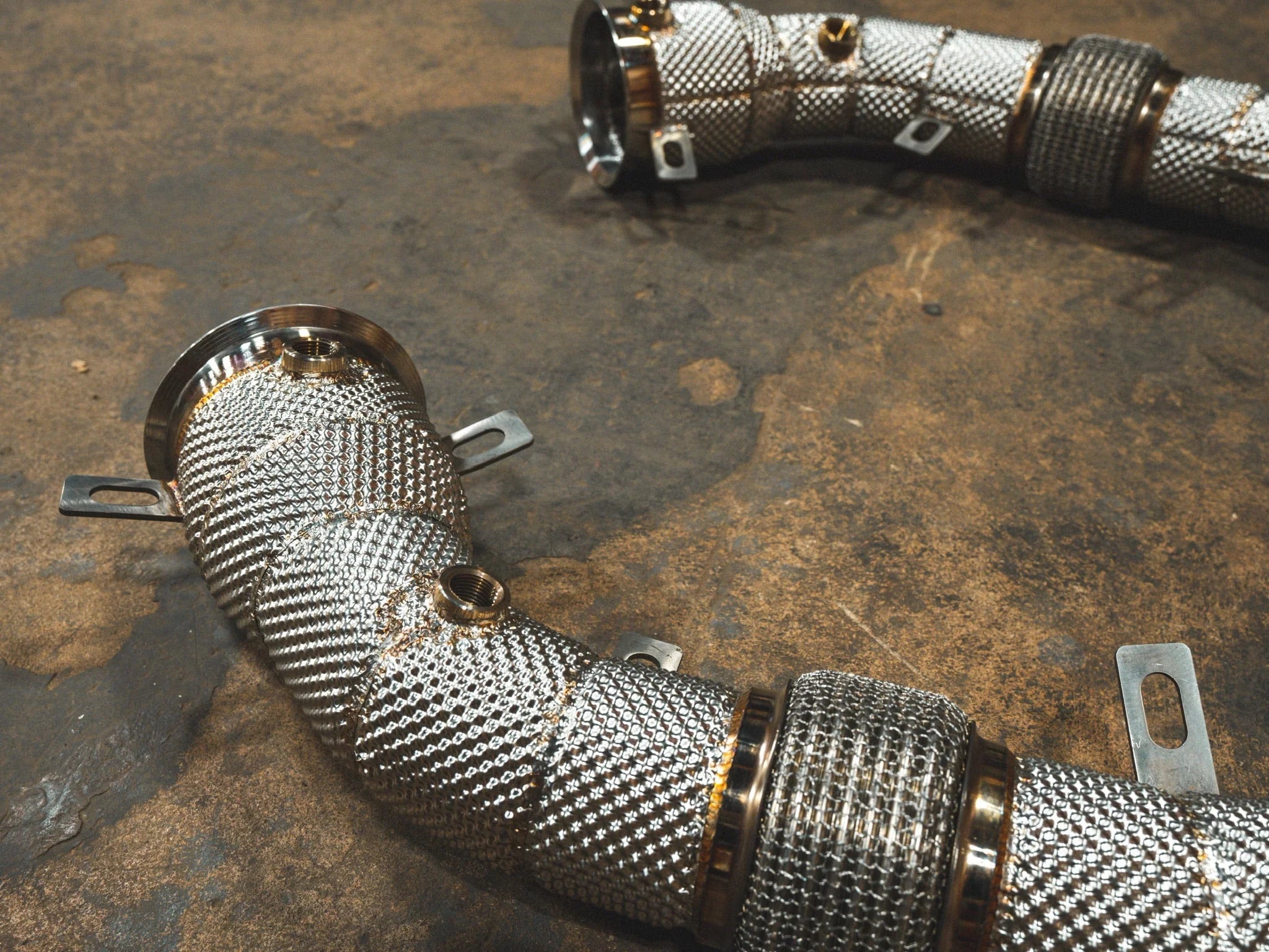 Close-up of the silver textured heat shielding and O2 sensor bungs on the exhaust downpipes.