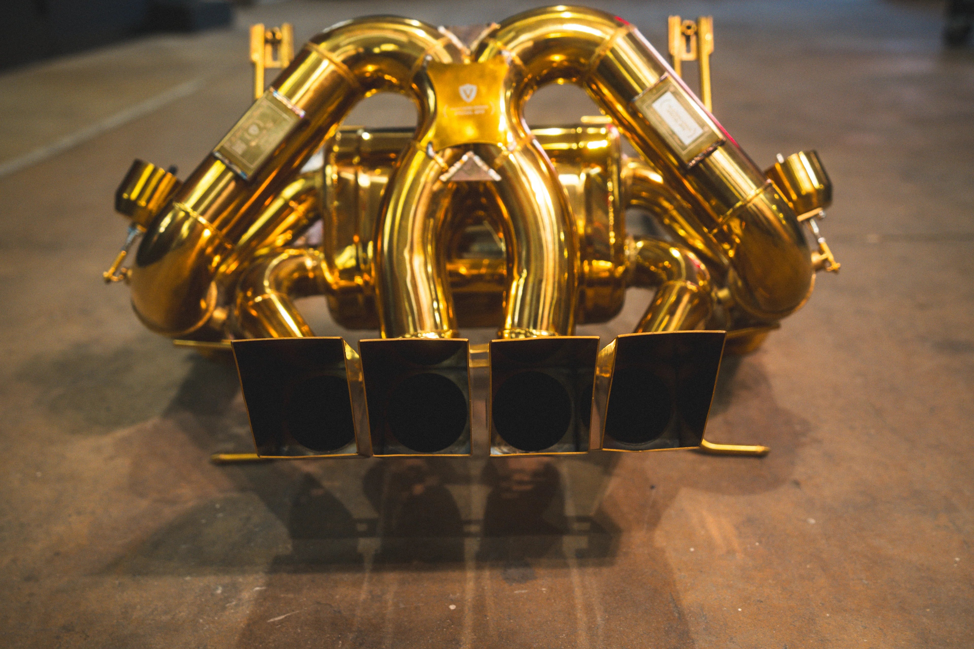 Low-angle rear view of the gold exhaust system focusing on the internal openings of the quad rectangular tips.