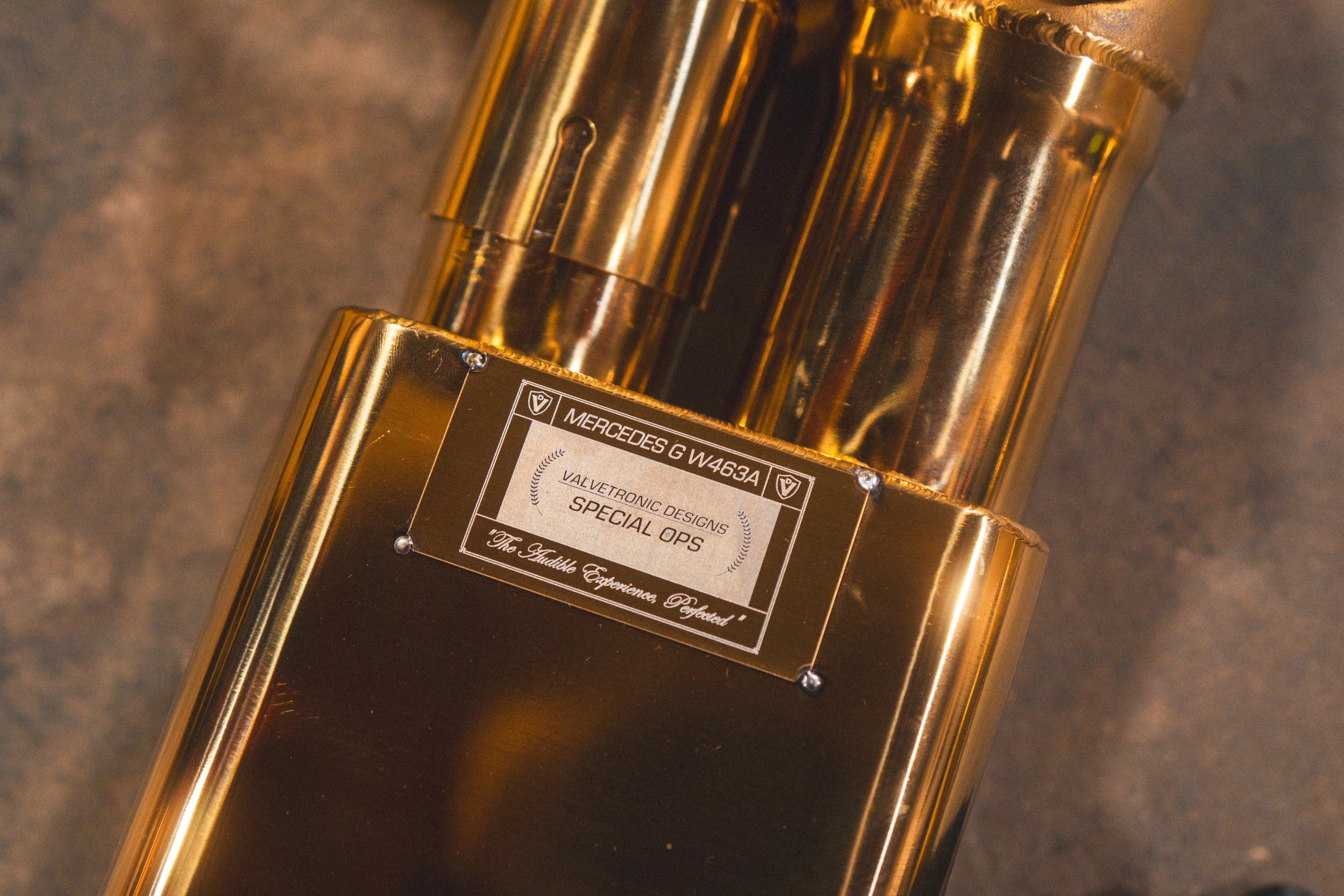 Detailed close-up of the "Special Ops" Valvetronic Designs identification plate riveted to the gold-finish muffler casing.