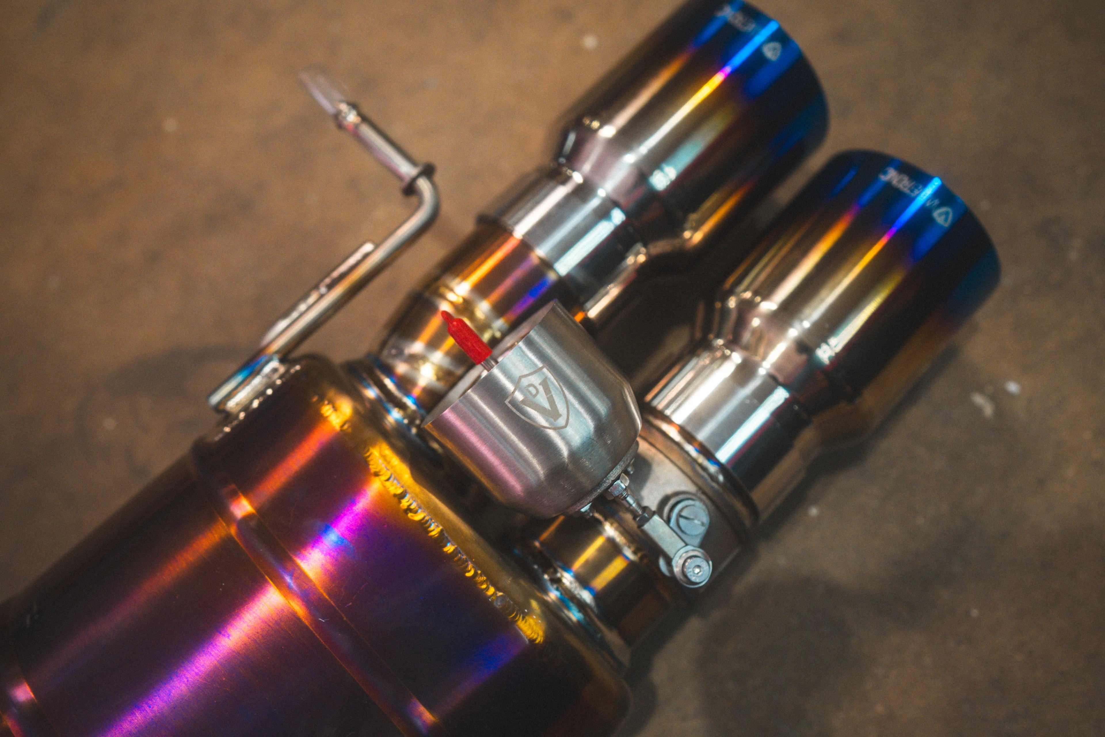 A macro view of a vacuum-actuated exhaust valve mounted on the piping near the burnt-blue exhaust tips.