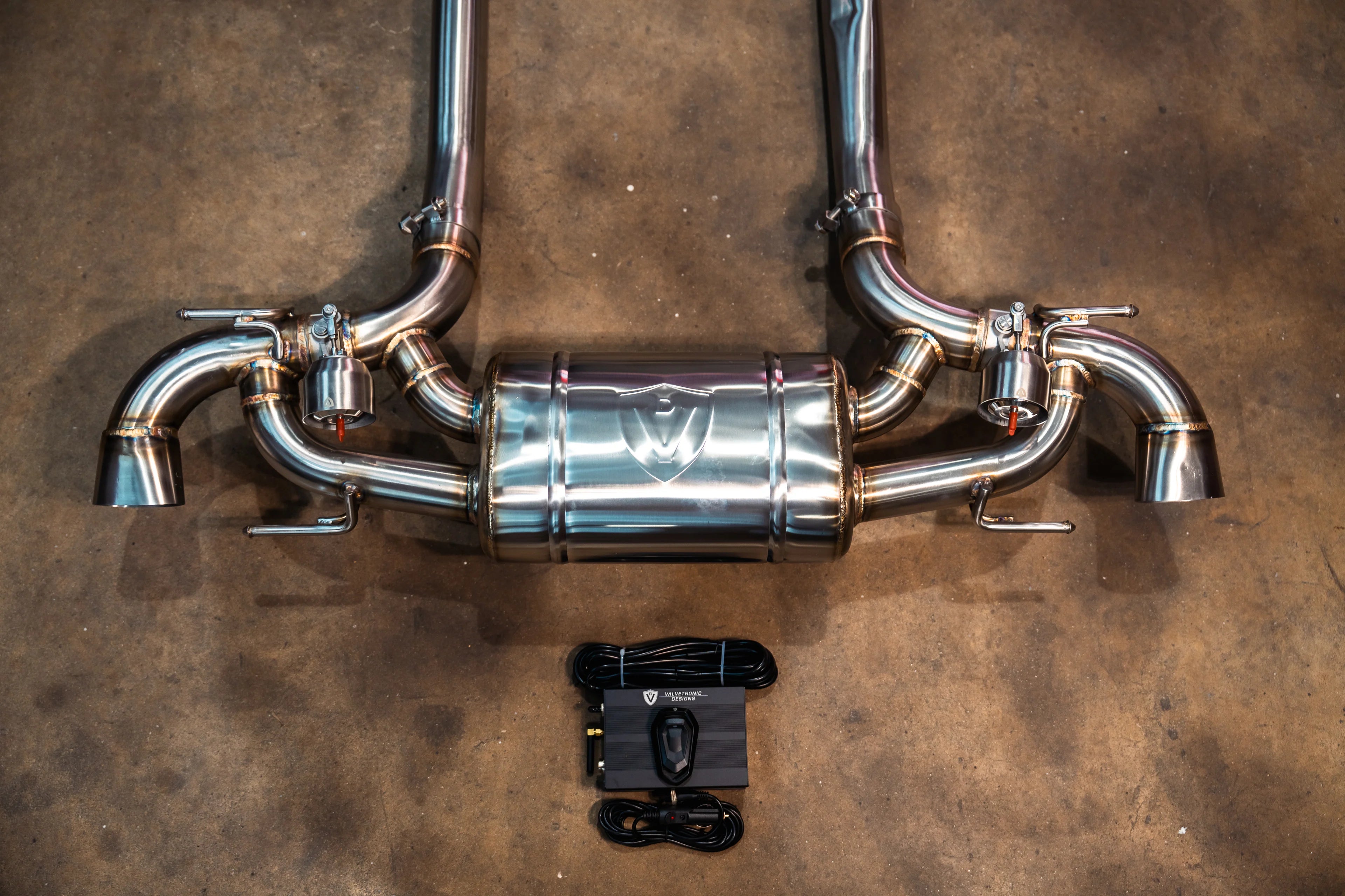 Overhead view of the complete Valvetronic rear exhaust assembly including the transverse muffler, valves, and the electronic control module with wiring.
