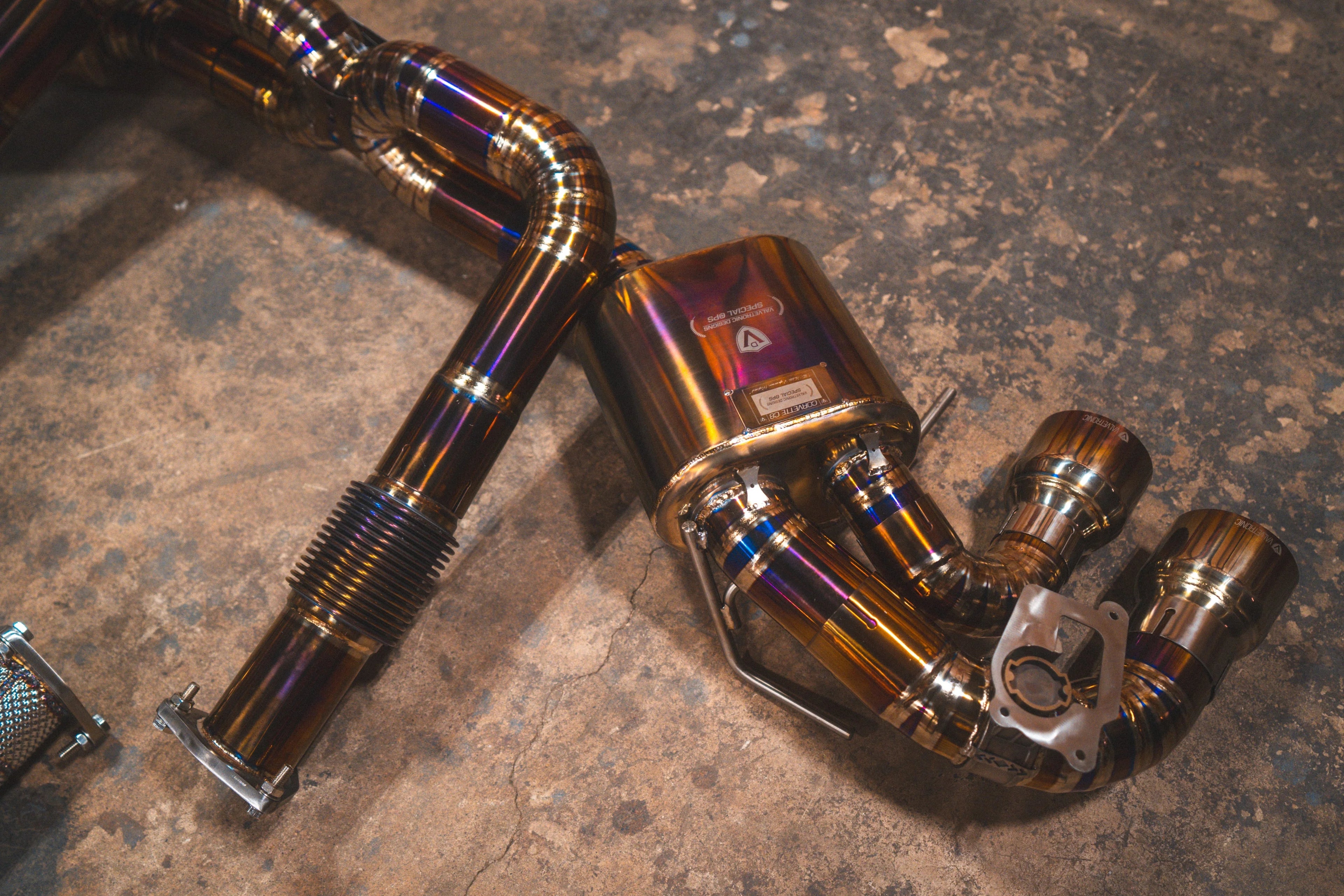 Detailed view of one side of the exhaust system, showing the transition from the flexible bellows to the muffler and the quad exhaust tips.