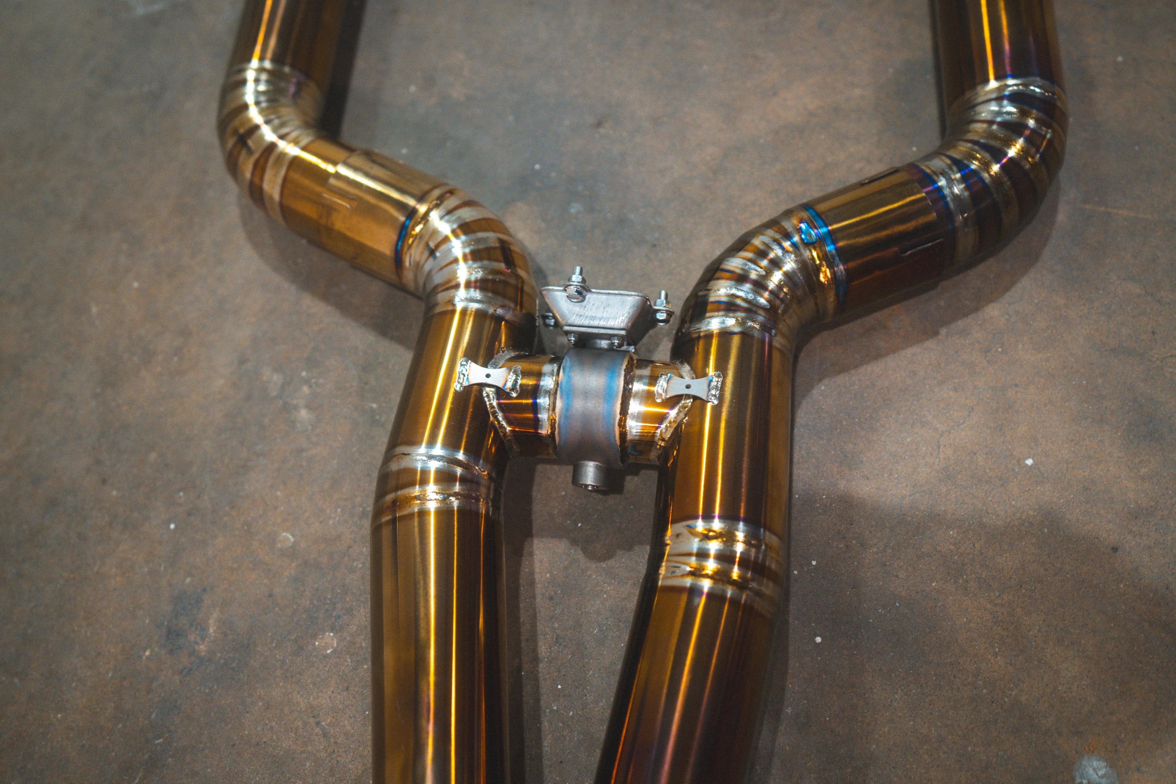Close-up of the exhaust system's H-pipe or crossover section featuring heat-tinted welds on the titanium piping.
