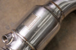 A close-up of the Valvetronic Designs 400 Cell Catted Downpipe focusing on the laser-etched identification plate on the brushed T304 stainless steel body.
