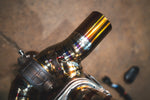 A close-up detail shot of a gold-finish exhaust pipe showing colorful heat discoloration and a robotic weld bead.