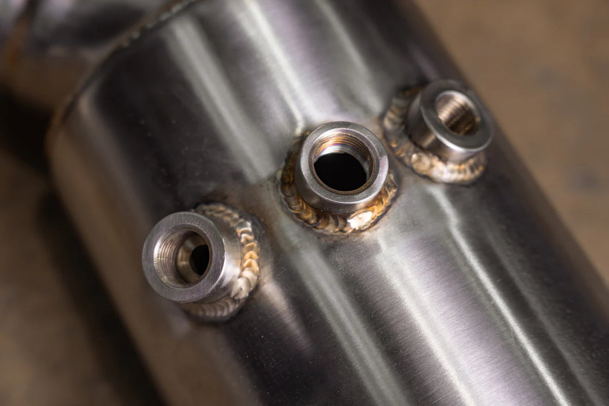 Detailed close-up of the Valvetronic Designs 400 Cell Catted Downpipe for the 2019-2022 Lamborghini Urus, showing three high-quality TIG-welded O2 sensor bungs on a brushed stainless steel surface.