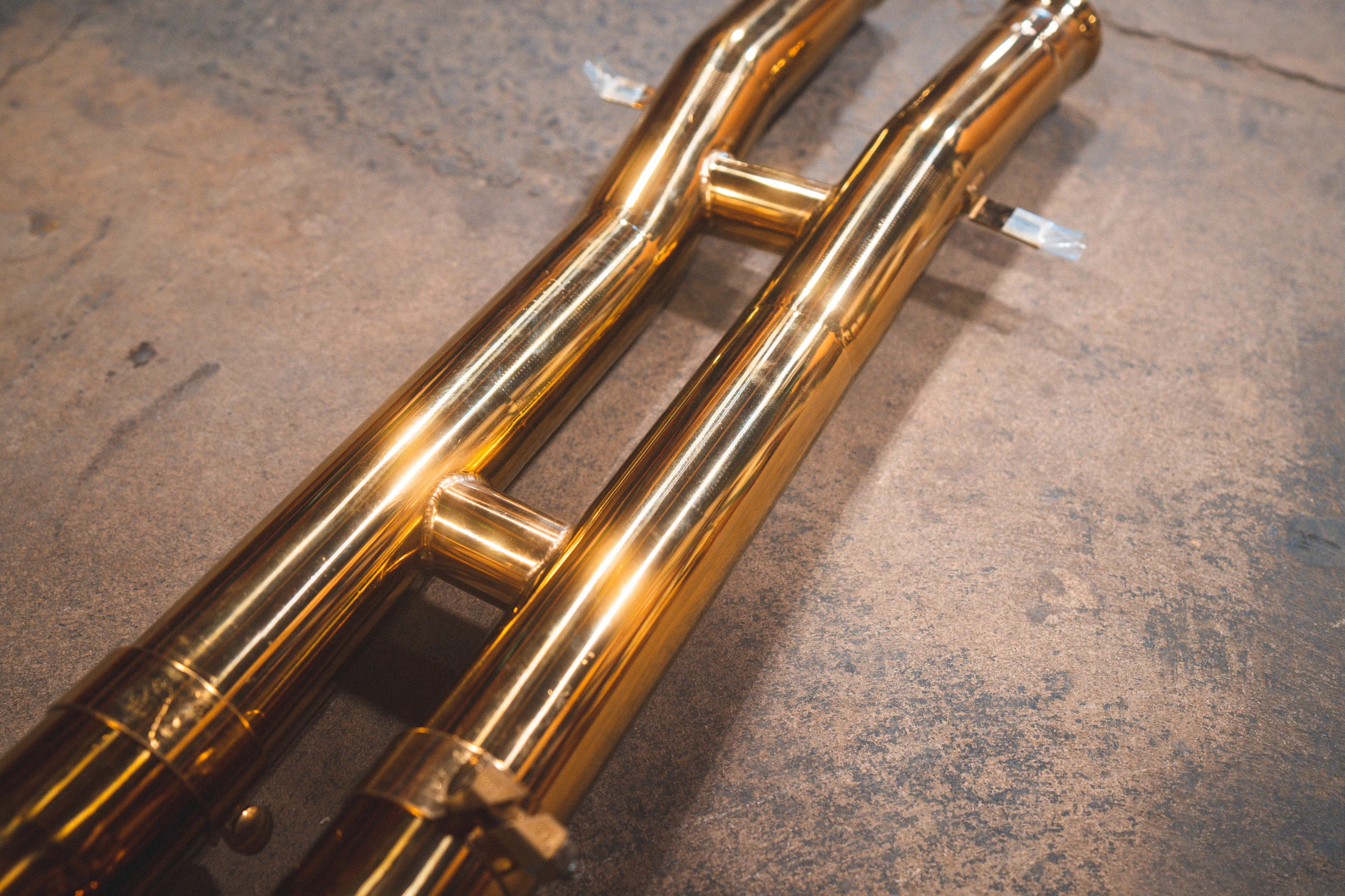 Perspective view of the dual mid-pipes showing the reflective gold finish and structural support braces.