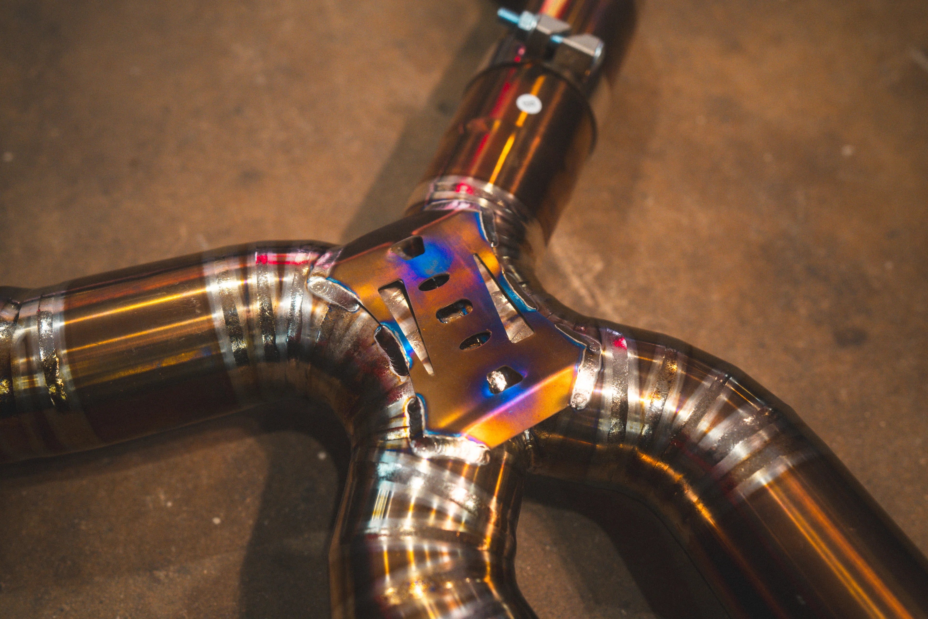 A close-up of the exhaust mid-section showing a support brace and the bolted clamps connecting the titanium pipes.