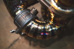 A macro shot of the precision TIG welding and purple-blue heat tinting on a curved section of the gold exhaust piping.