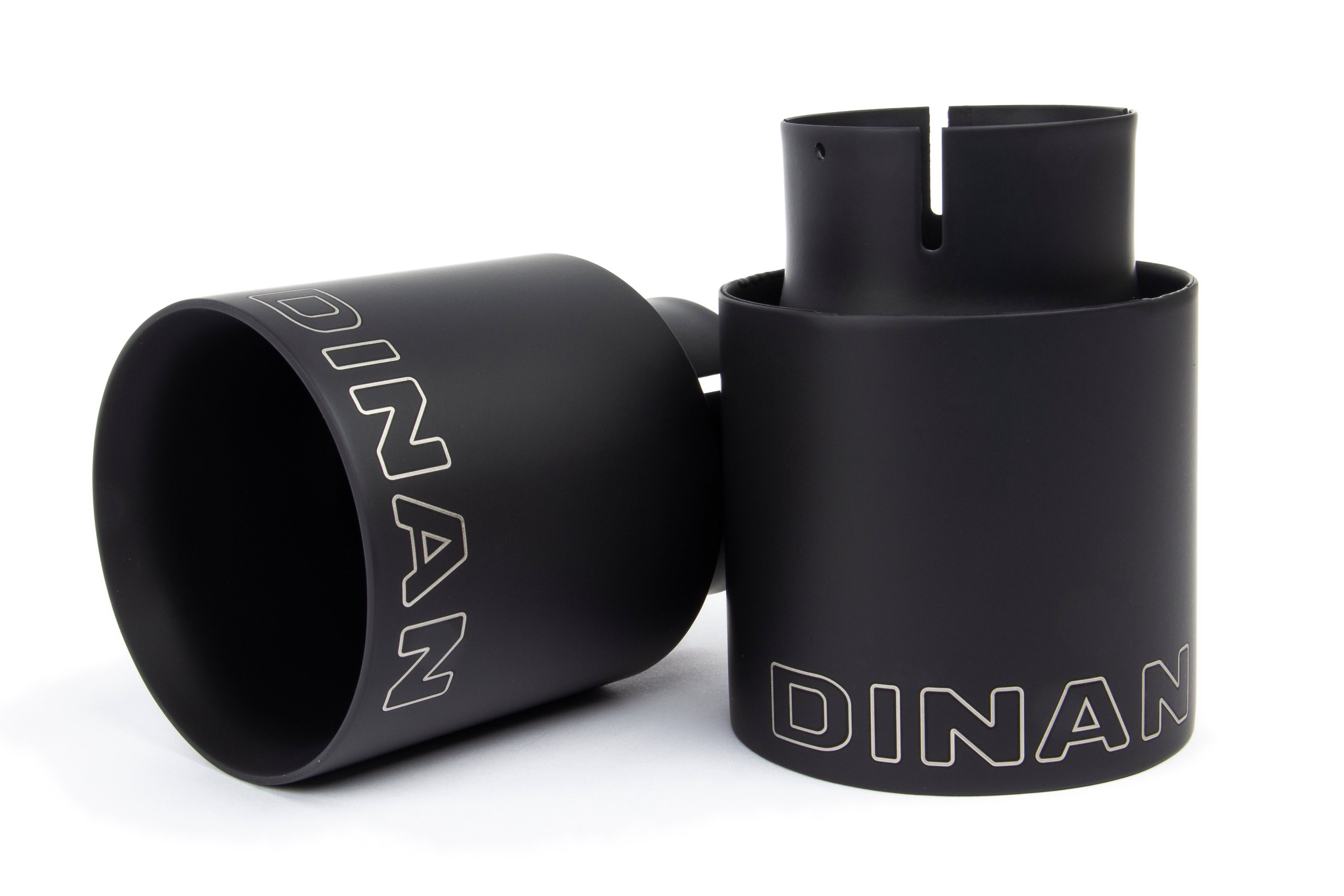 A close-up view of the two black ceramic coated exhaust tips. The image highlights the double-walled, slant-cut design with a mirror finish and the laser-etched Dinan logo on the top of each tip.