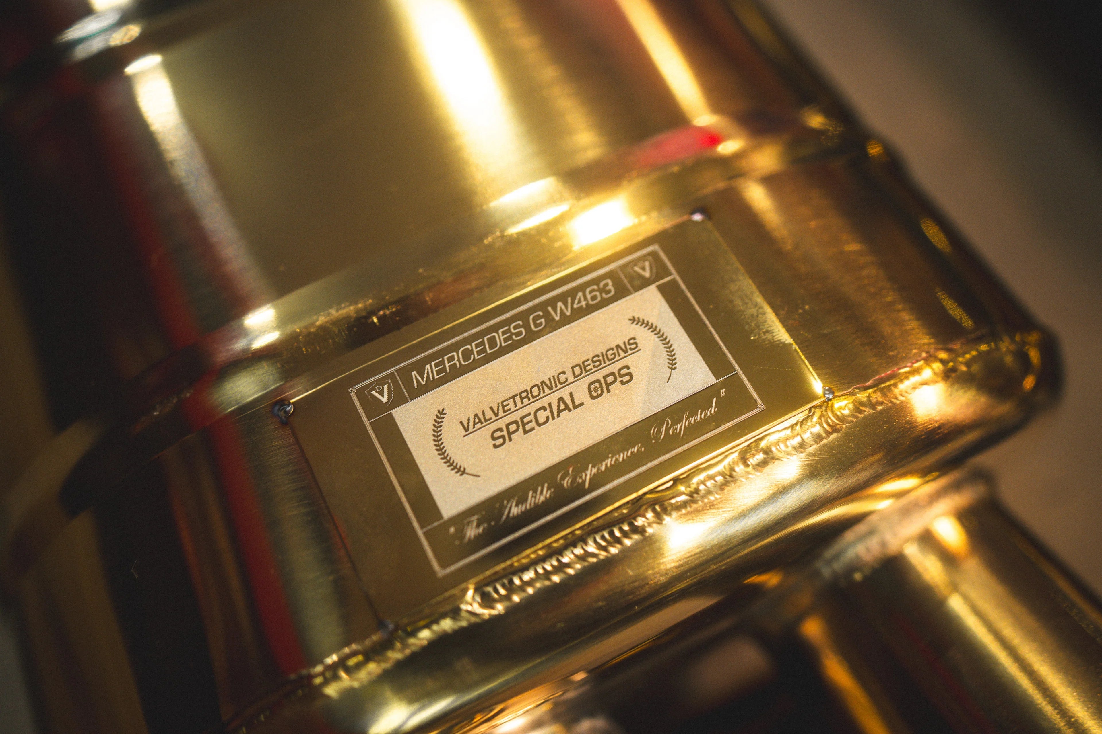 Detailed macro shot of the "Special Ops" Valvetronic Designs identification plaque welded onto the gold-finish muffler body.