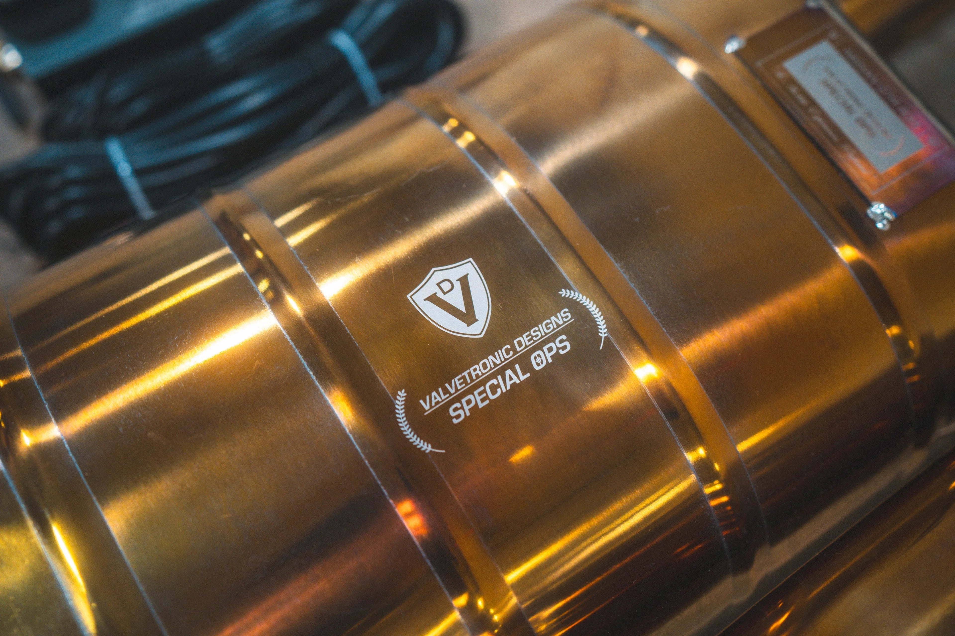 Macro shot of the "Valvetronic Designs Special Ops" branding and serial number plate on the polished gold-finish muffler body.