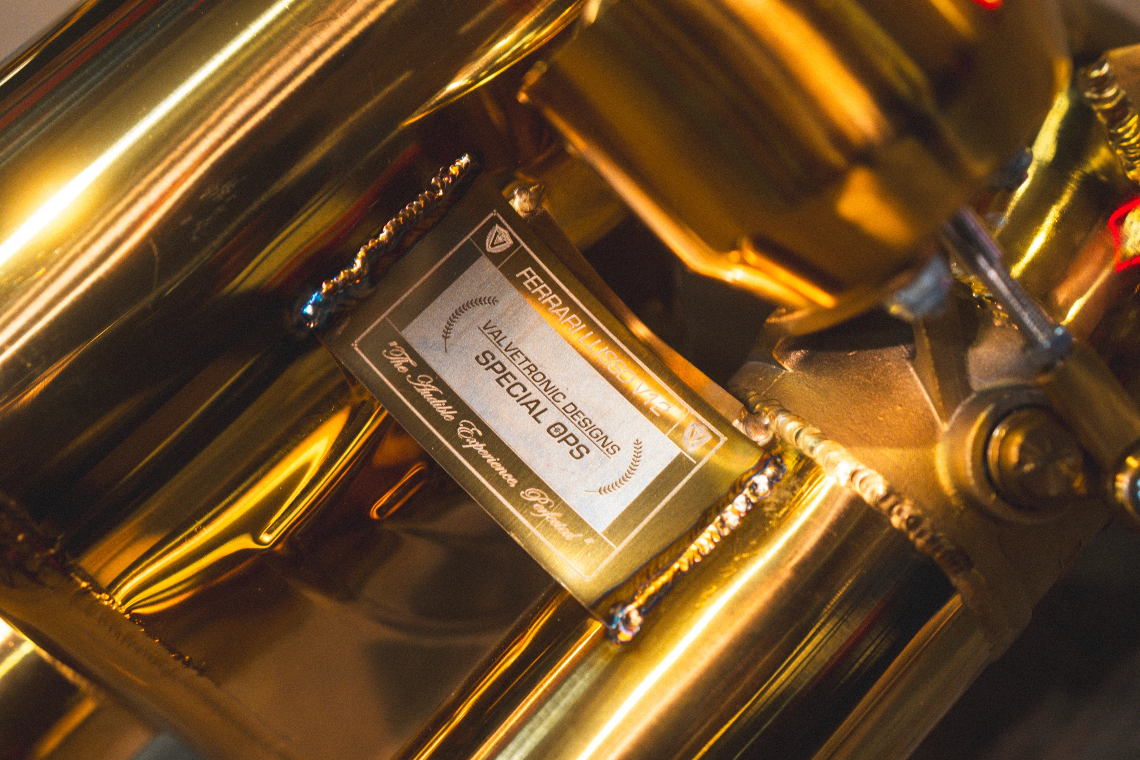 A macro shot of precision TIG welding and purple-blue heat tinting on a curved section of gold exhaust piping.