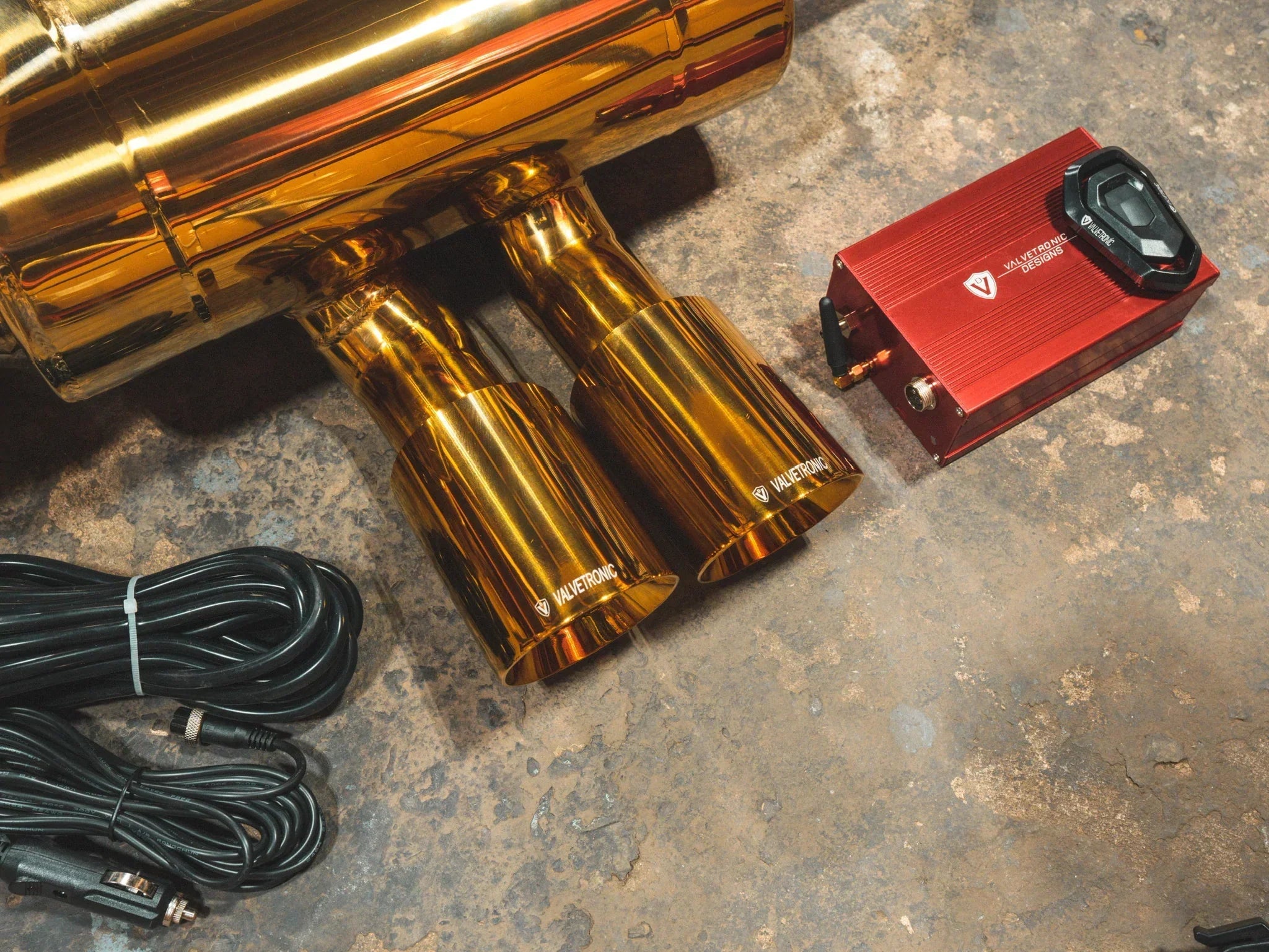 Detail shot of the polished gold dual exhaust tips with the Valvetronic logo next to the red electronic valve controller and remote.