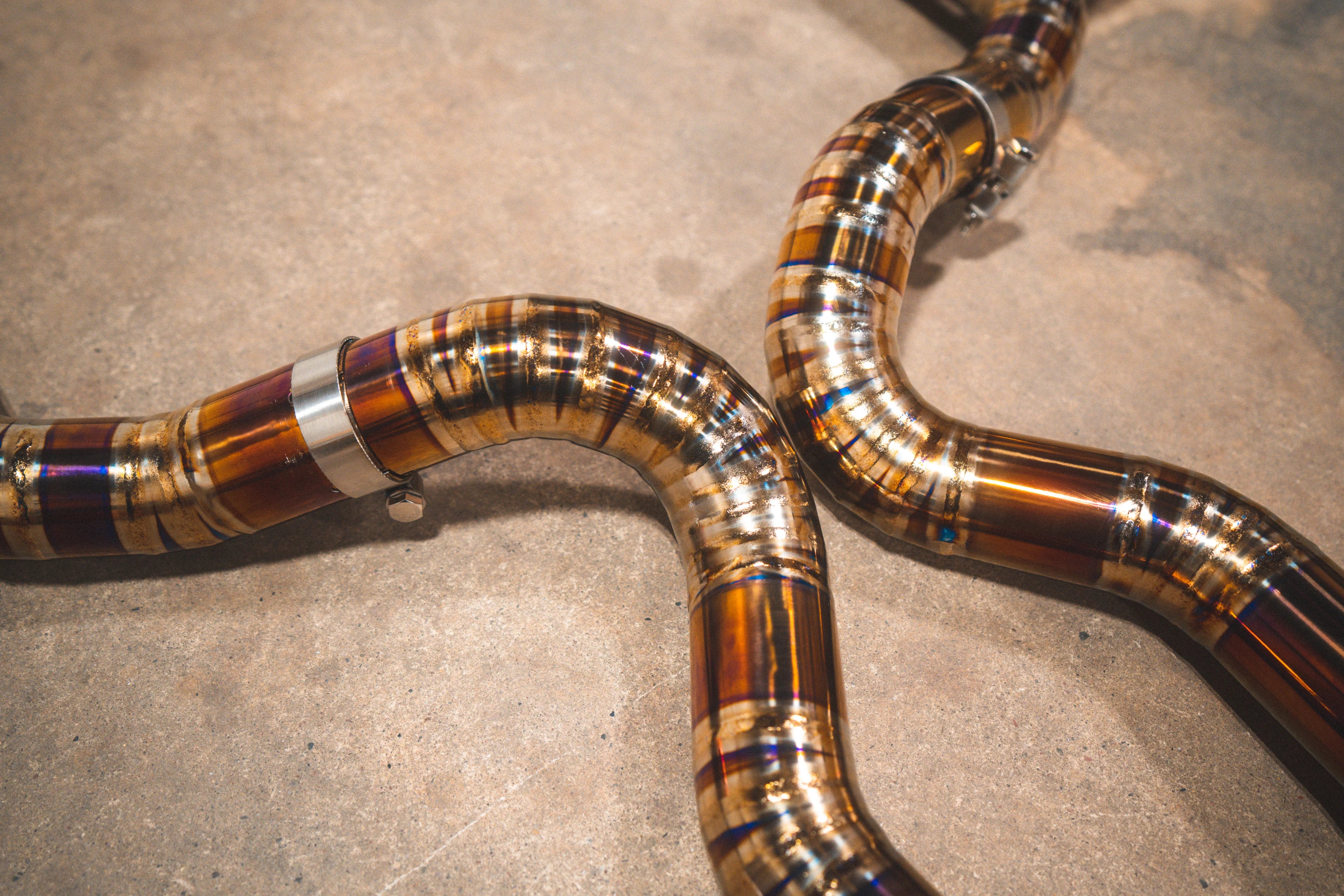 Close-up showing the curved titanium piping with blue and purple heat discoloration on the welds.
