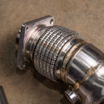 A close-up of a Valvetronic Designs 400 Cell Catted Downpipe focuses on the stainless steel interlock flex section and the thick mounting flange. 