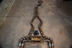 A full titanium valved exhaust system with a heat-treated bronze finish and quad tips laid out on a concrete floor with a black controller kit.