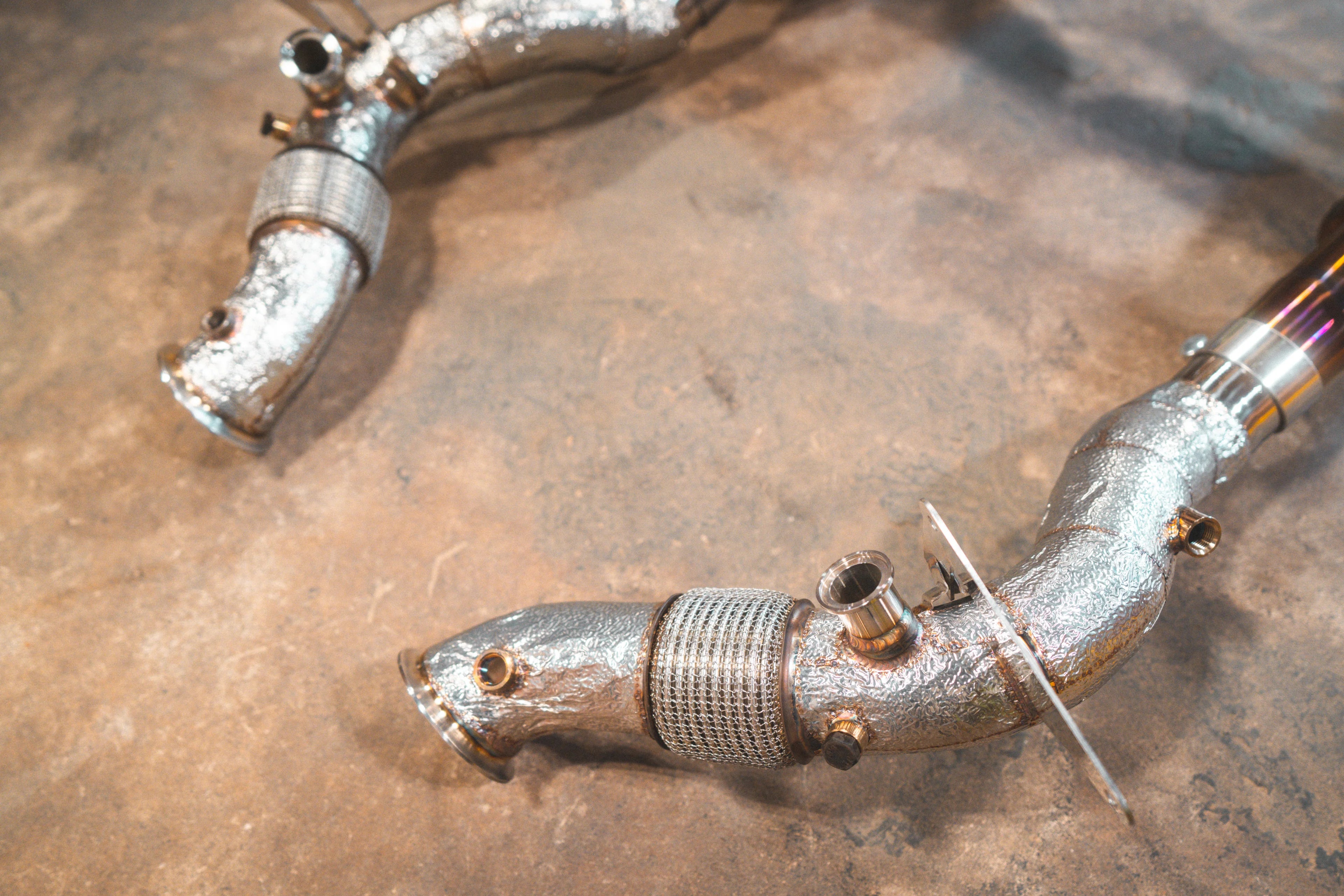 A close-up view of the stainless steel 4-into-1 exhaust headers connected to a silver mid-pipe with textured heat shielding.