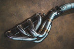 A close-up view of the stainless steel 4-into-1 exhaust headers and the connection to the heat-shielded mid-pipe.