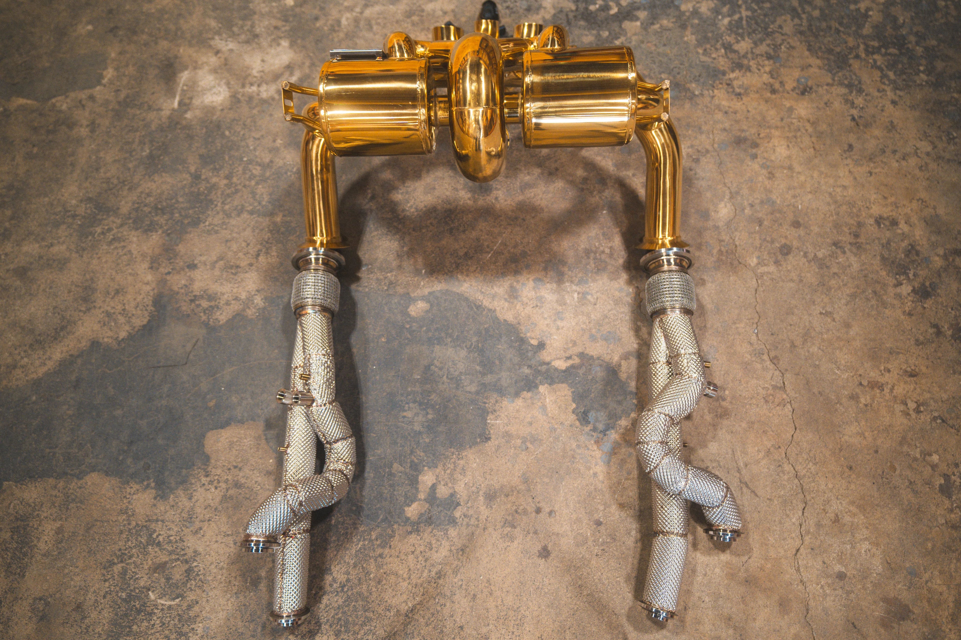 Underside view of the gold-plated exhaust assembly highlighting the symmetrical piping and silver braided heat shielding.