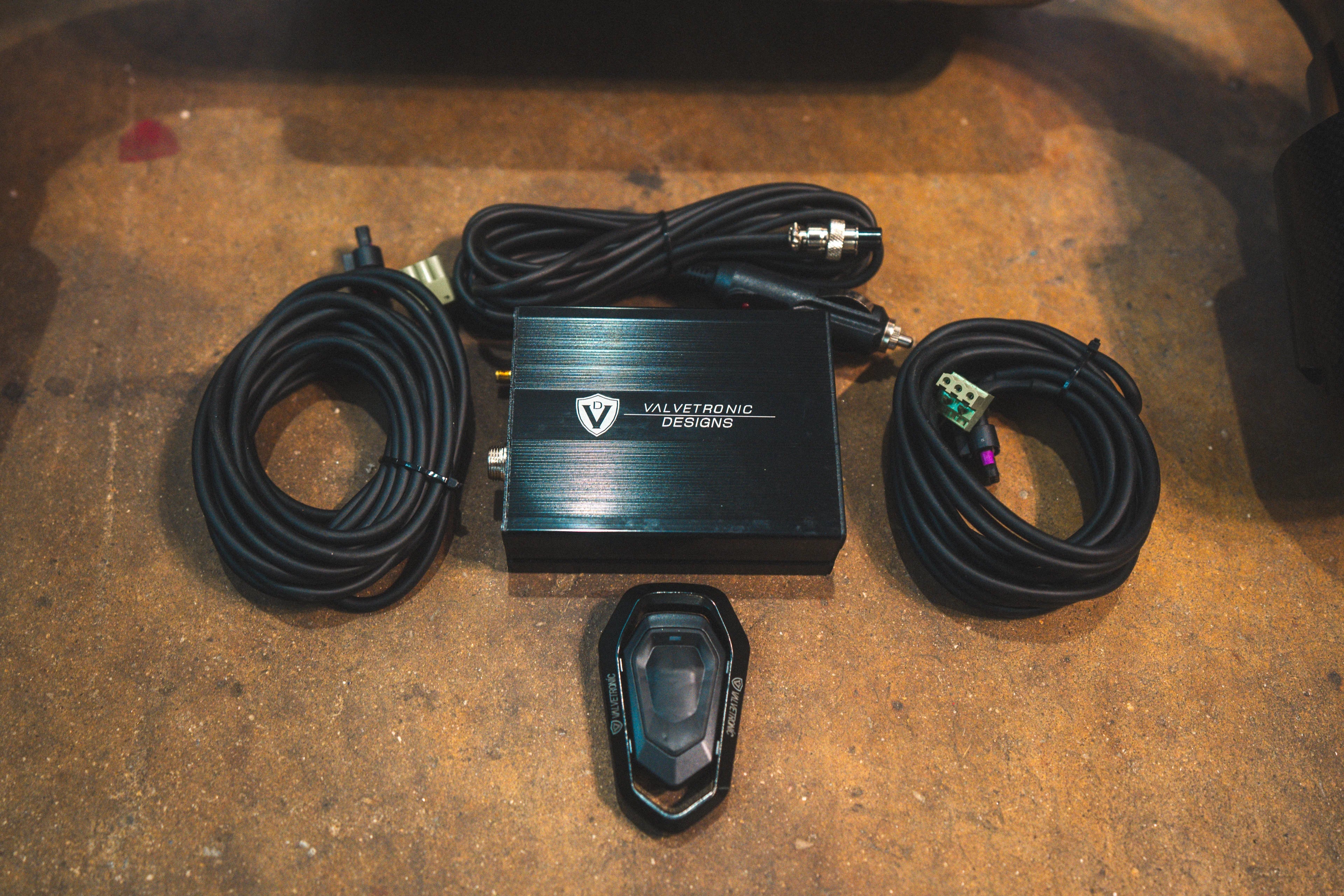 Overhead view of the valve controller kit including the electronic control box, wiring harnesses, and remote key fob.