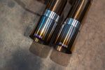 Detailed view of two burnt-finish titanium exhaust tips featuring the Valvetronic logo on a concrete workshop floor.